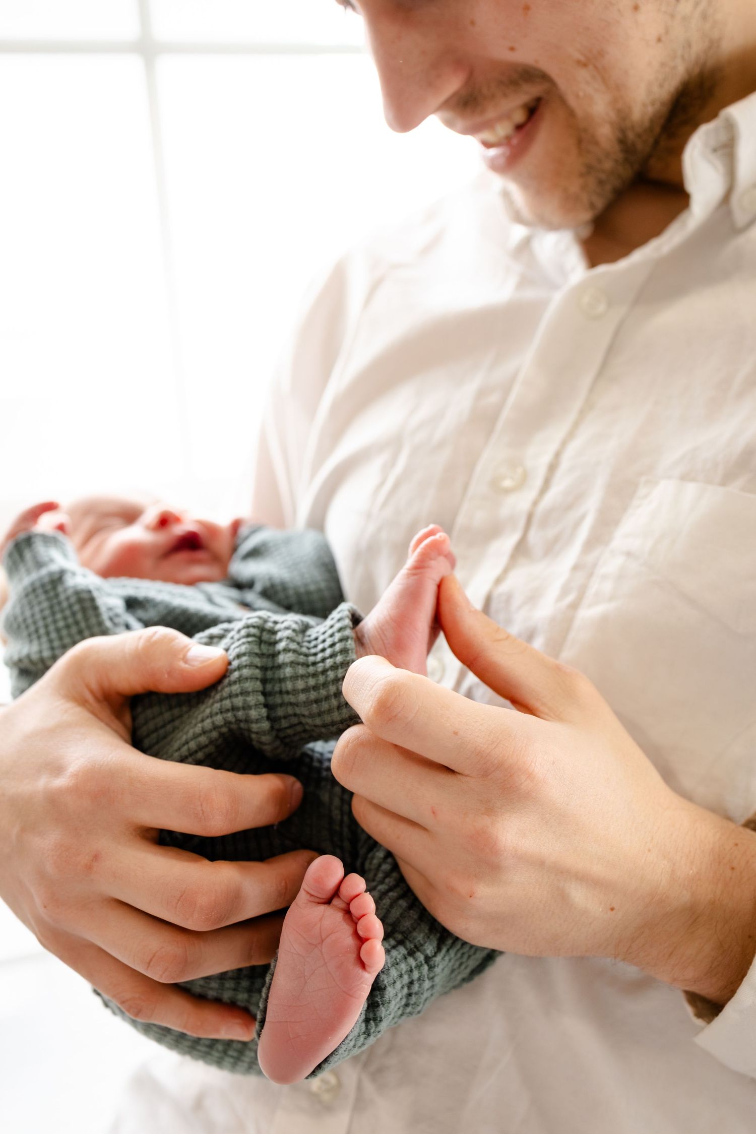 Father gazes at their swaddled newborn baby in a bright, minimalist setting during Indianapolis in-home newborn photography session