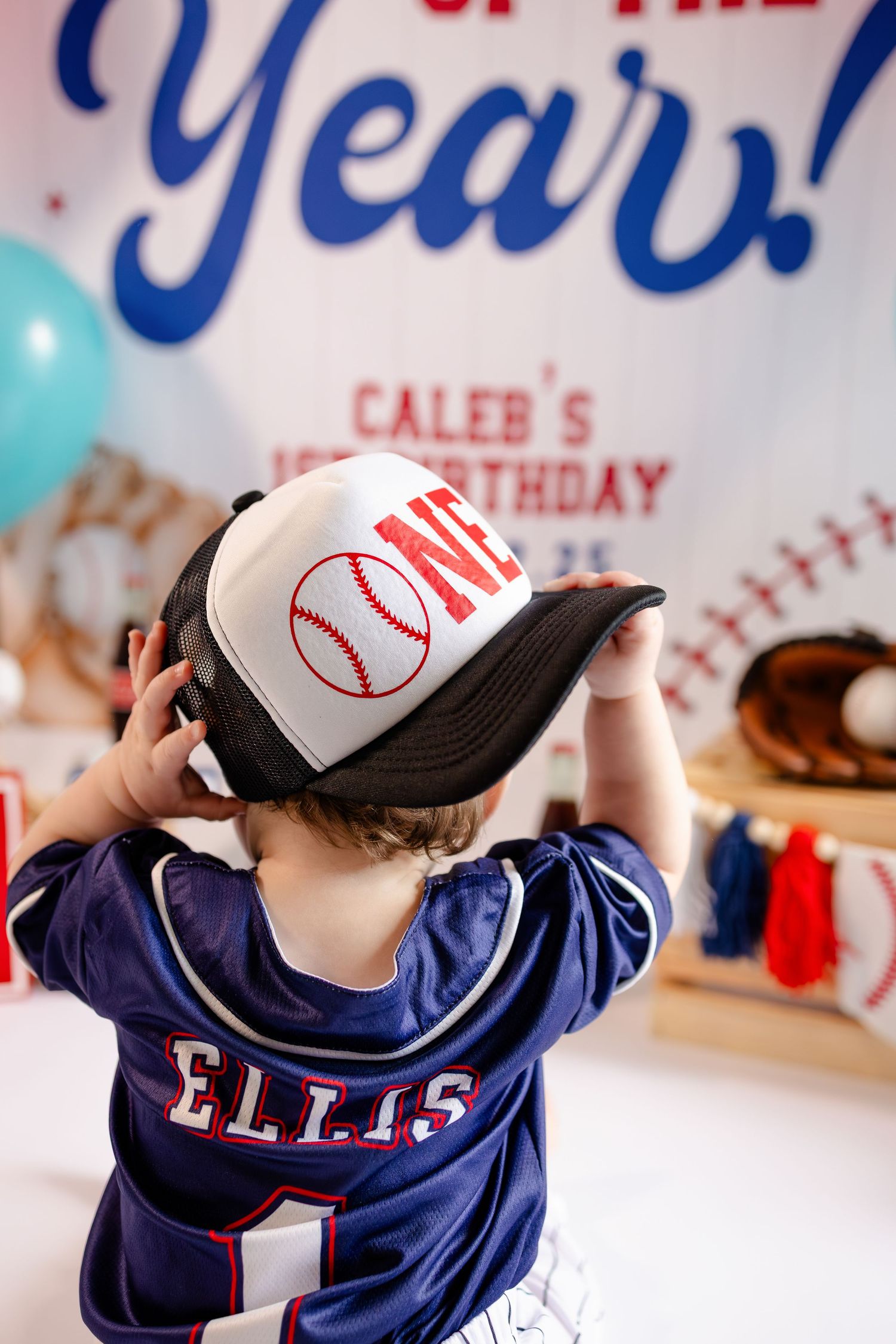 A baseball-themed party display with navy blue jerseys and white baseball caps for first birthday session in Brownsburg, IN.