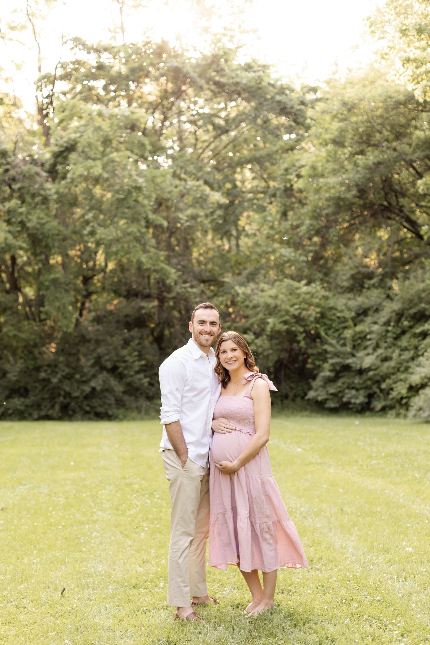 Couple embracing in a sunlit meadow with trees in the background.
