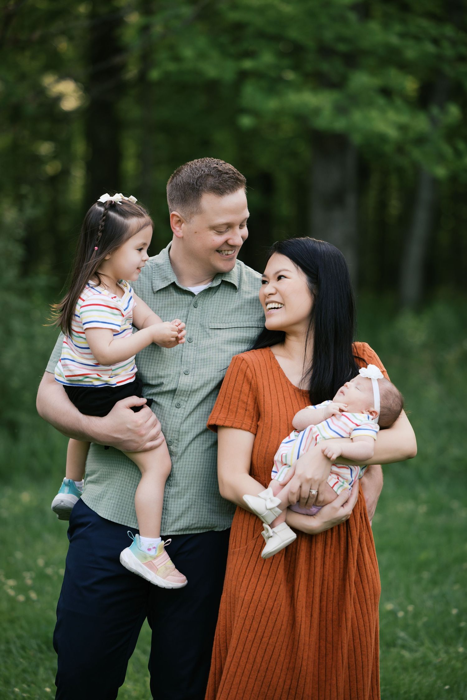 Happy family of four outdoors, parents holding toddler and newborn baby, smiling in a park  for Brownsburg, Indiana Family Photo Session.