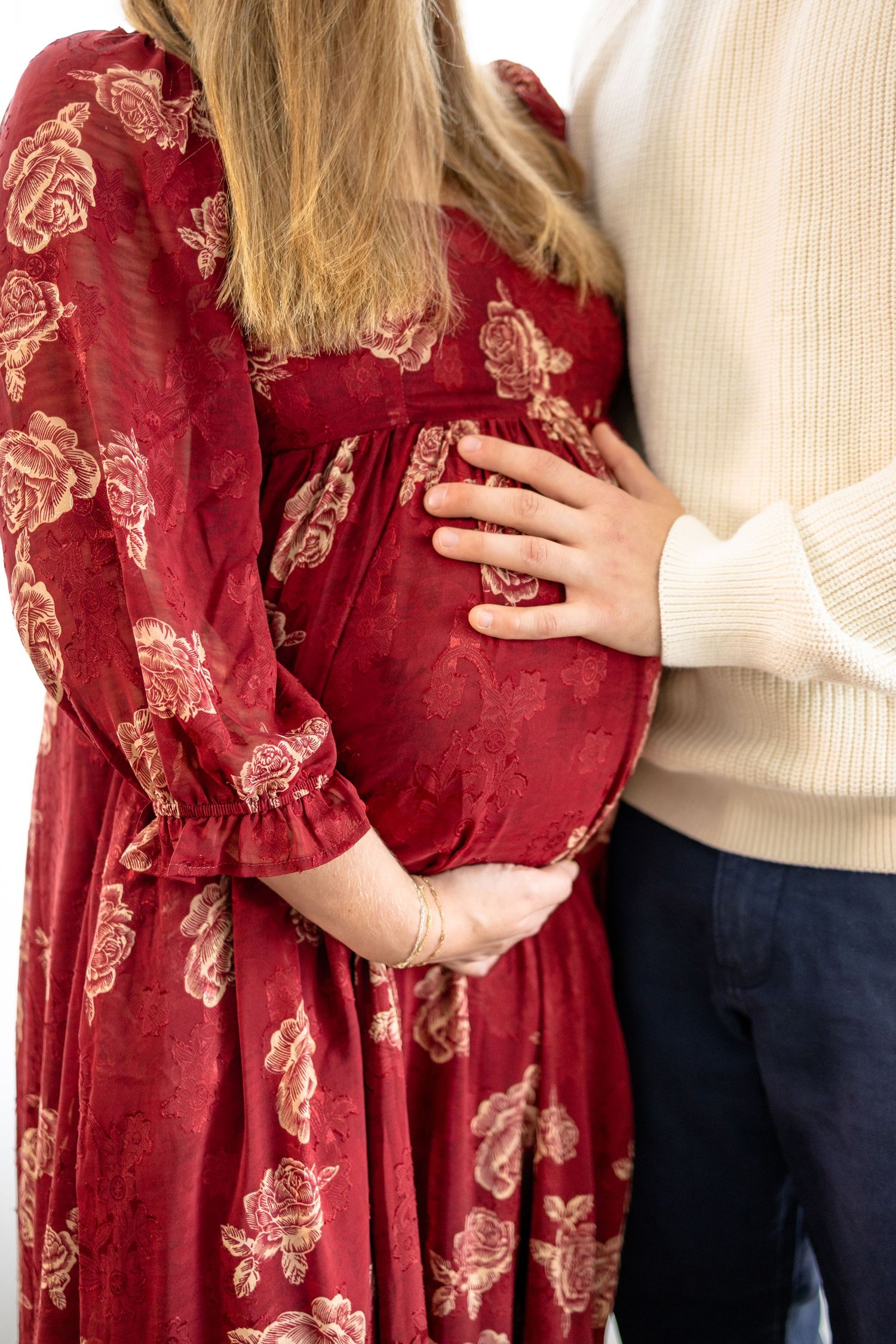 A couple poses together showing a burgundy floral dress and white sweater in an intimate maternity photoshoot in Brownsburg, Indiana.