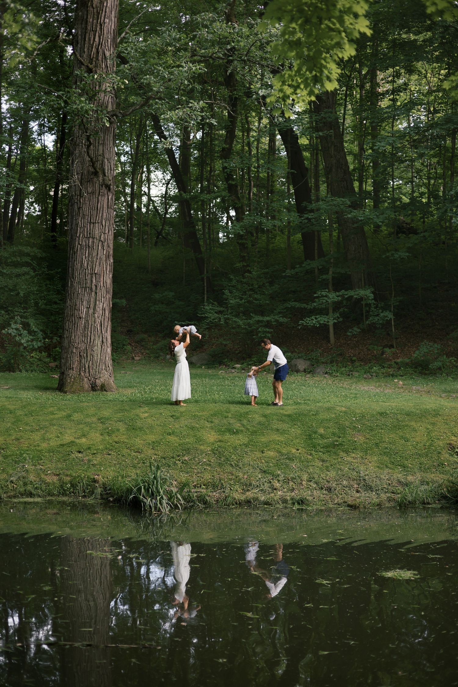Family playing near a pond surrounded by green trees in a peaceful park setting at Indianapolis Family Session by Katy Rose Photography.