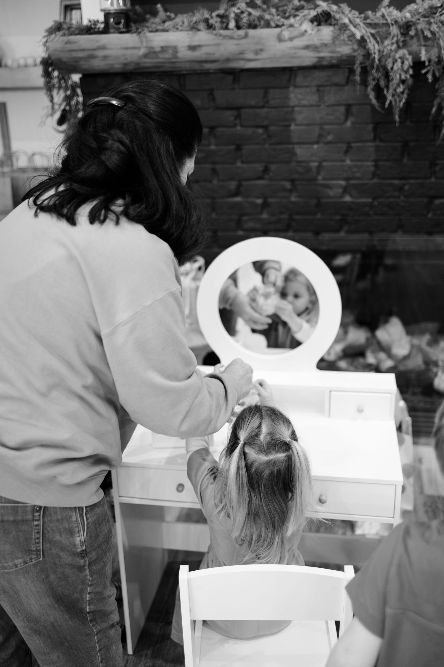 Black and white photo of a child and adult at a white vanity mirror during in-home lifestyle session in Whitestown, Indiana.