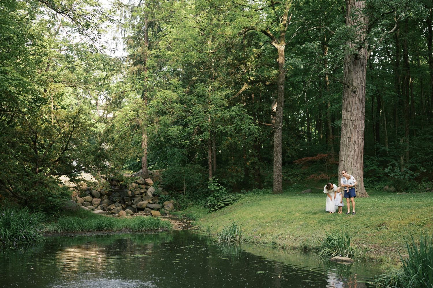 Family by a pond surrounded by green trees in a beautiful woodland garden setting for Indianapolis Family Session by Katy Rose Photography.
