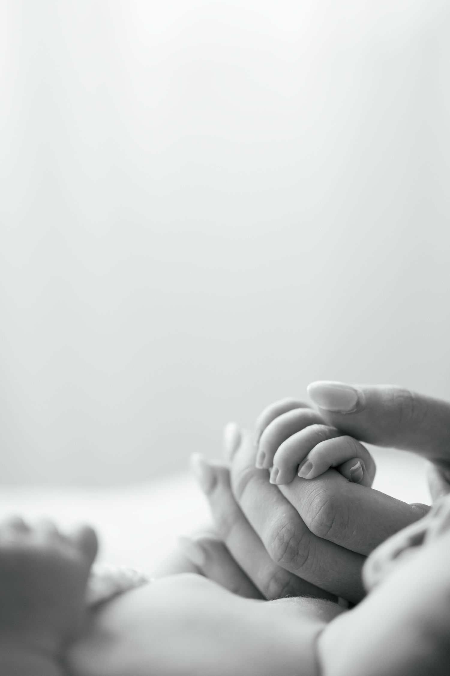 Black and white photo of a newborn baby grasping a mother's finger, symbolizing love and new life.