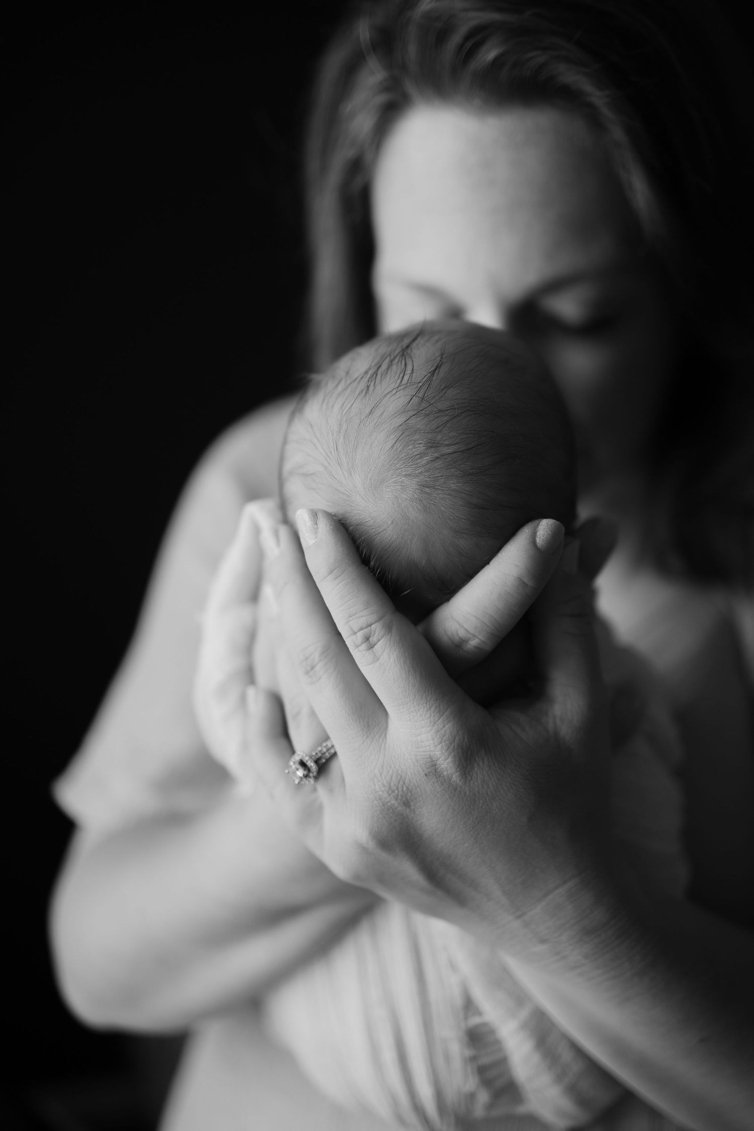 Black and white photo of a mother tenderly cradling her newborn baby's head during in-home newborn session in Hendricks County