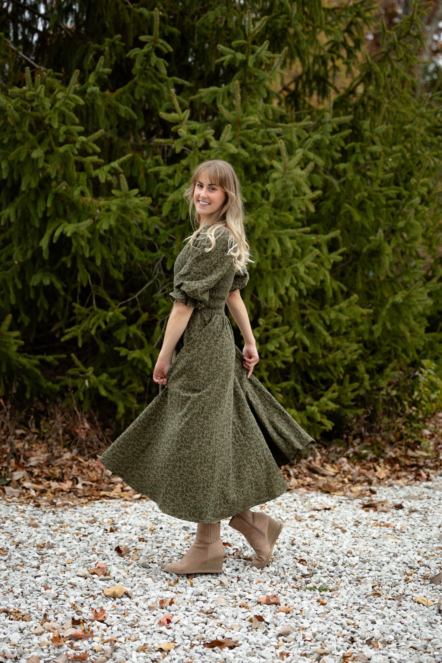 Twirling in vintage-style green dress against evergreen trees in winter setting for Avon Photographer Branding Session.