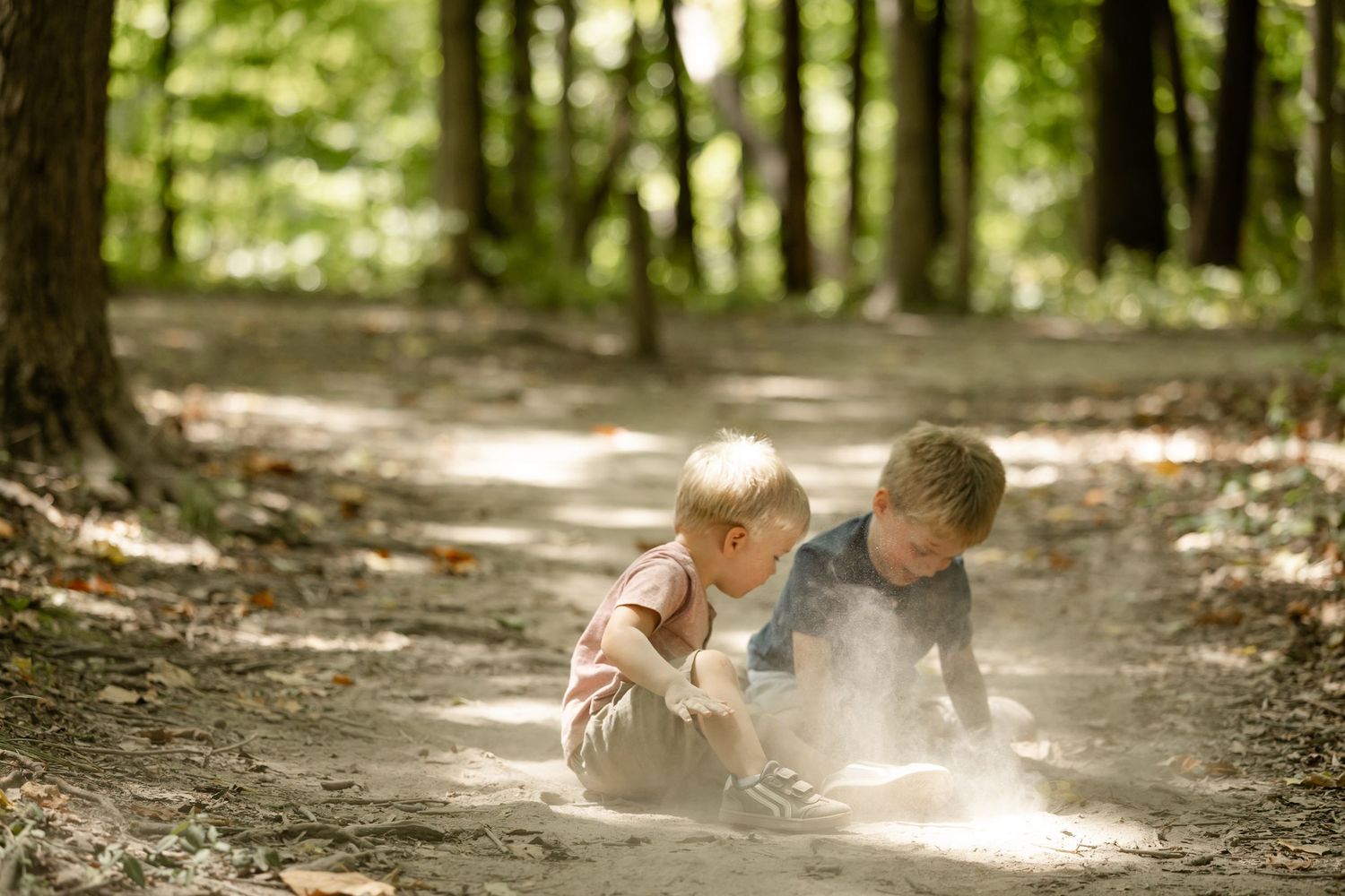 Two young children playing in sandy dirt on a forest path surrounded by green trees at Washington Township Park in Avon, Indiana.