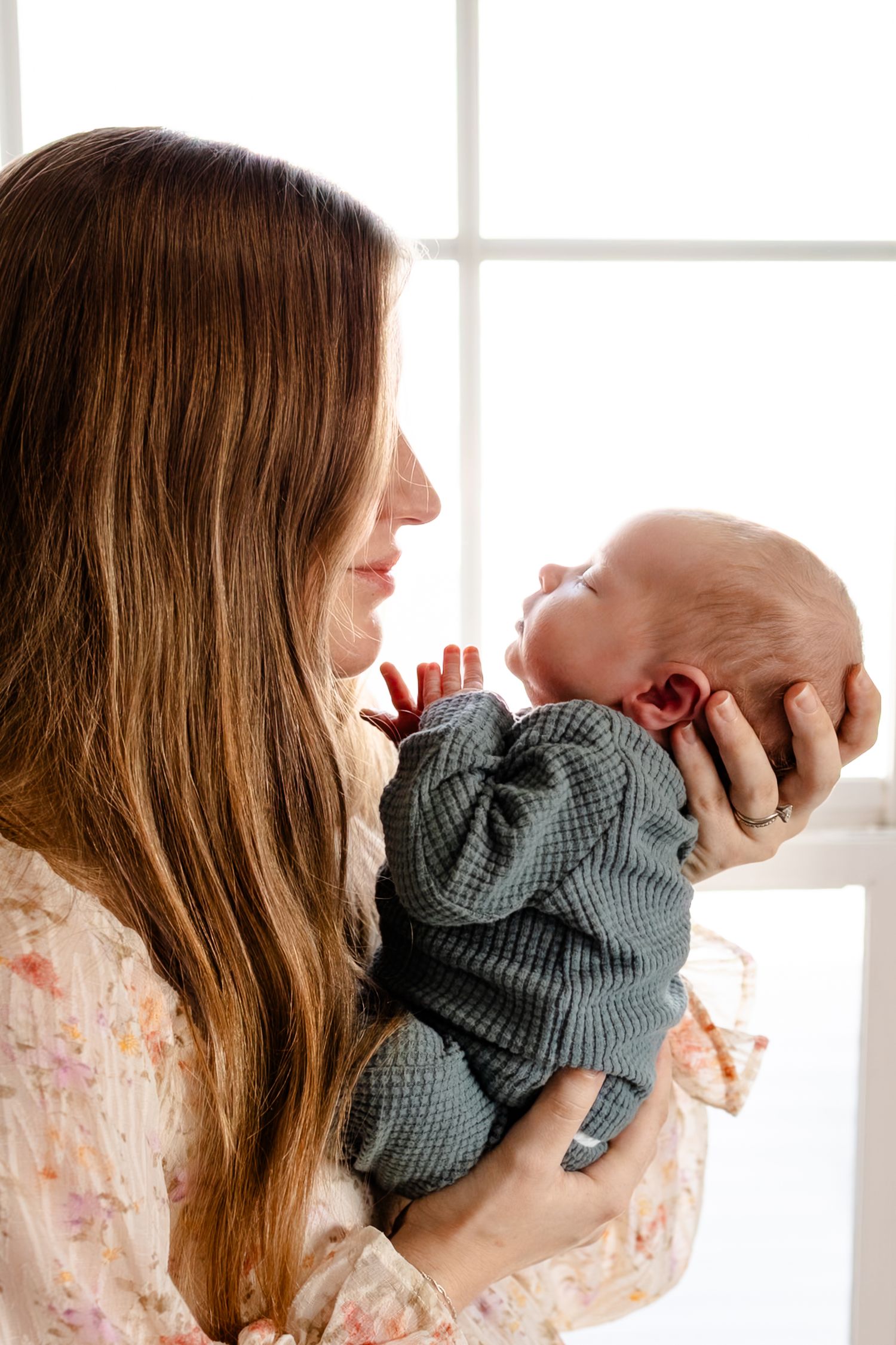 A mother holding her newborn in front of her in front of windows at in-home newborn photoshoot in Indianapolis by Katy Rose Photography