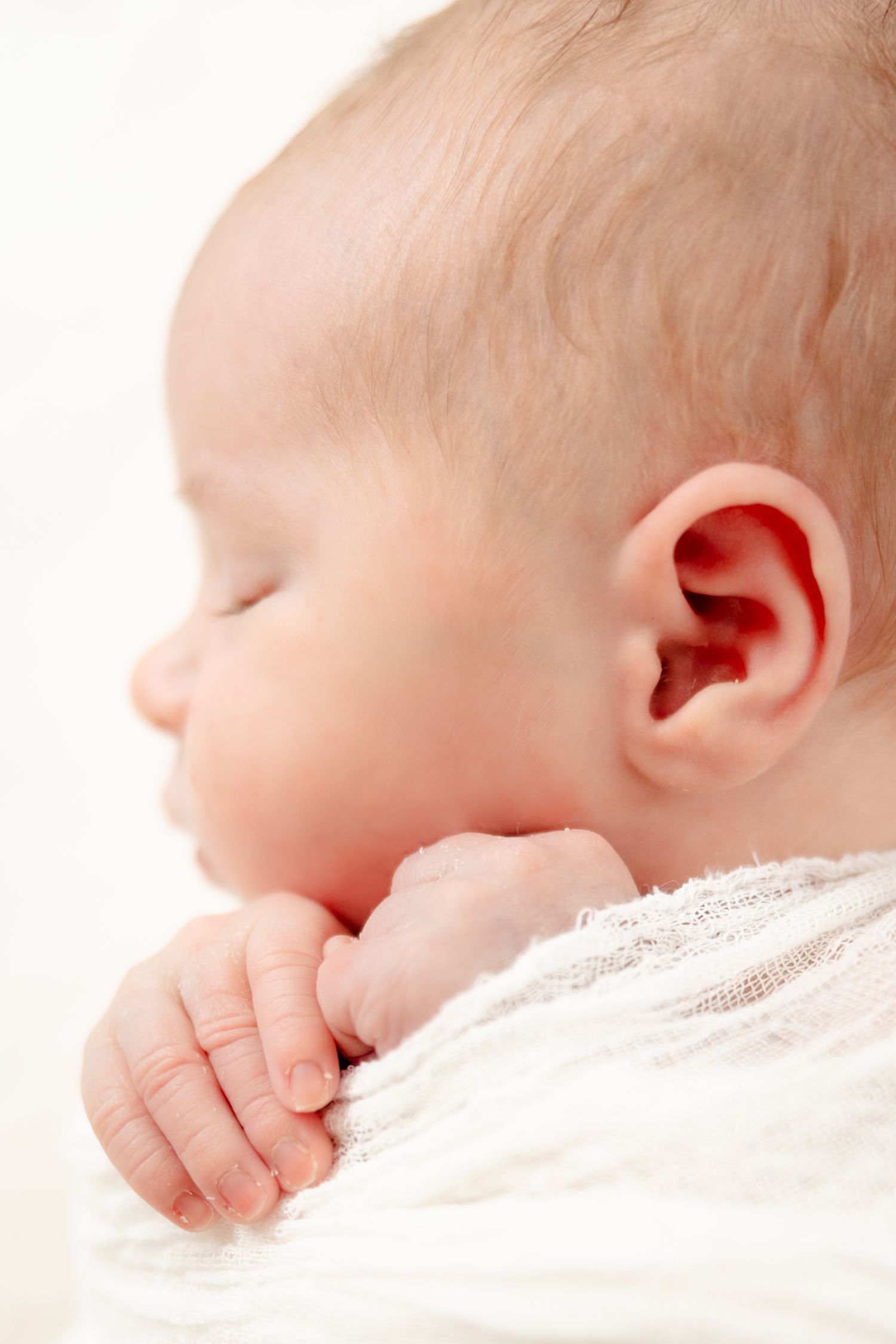 Close-up profile view of a sleeping baby's head and tiny hand against soft white fabric during newborn session in Indianapolis