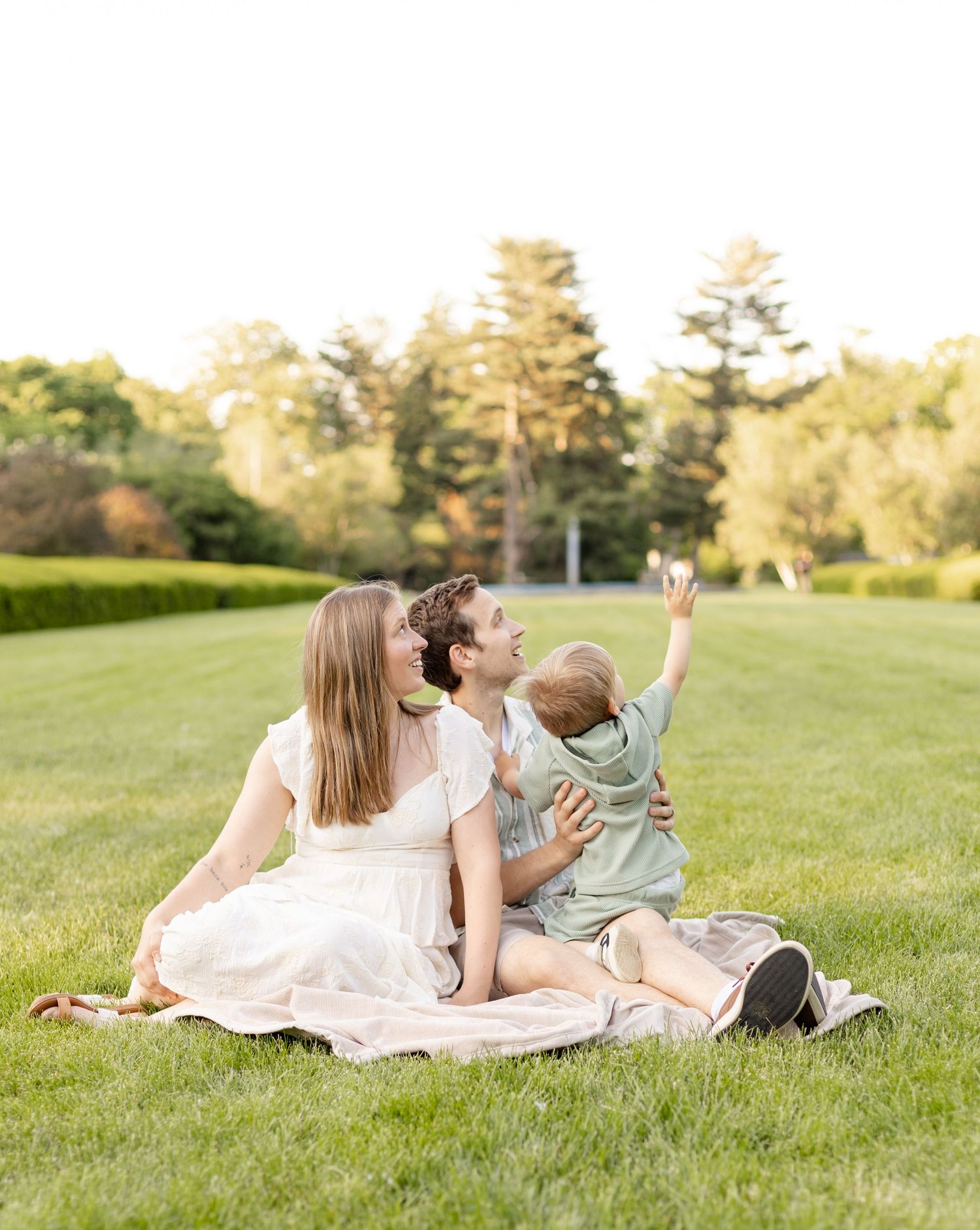 A family sitting together on a grassy hill during a sunny afternoon family photoshoot at Holcomb Gardens in Indianapolis.