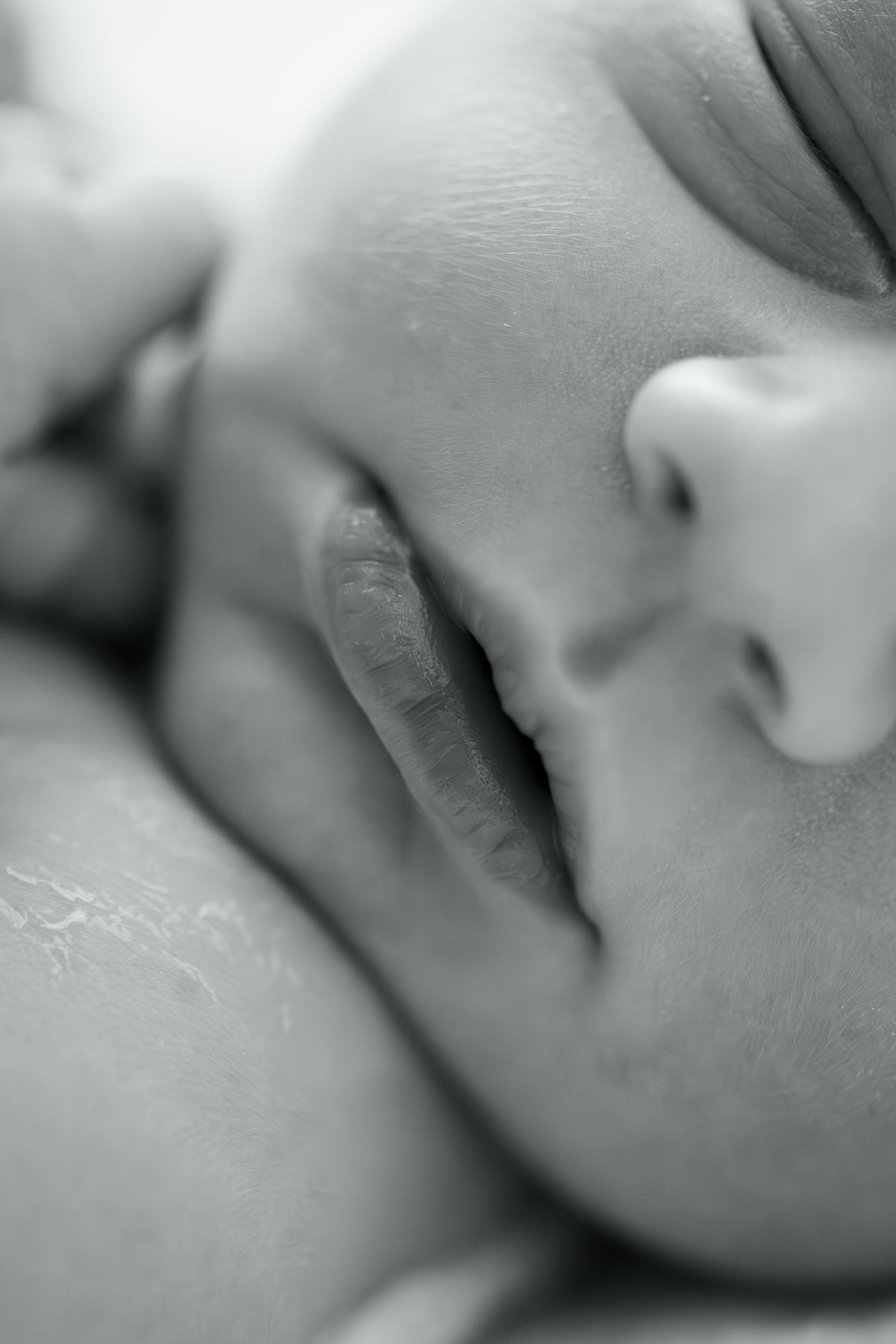 Close-up black and white photo of a sleeping newborn baby with tiny fingers near face.