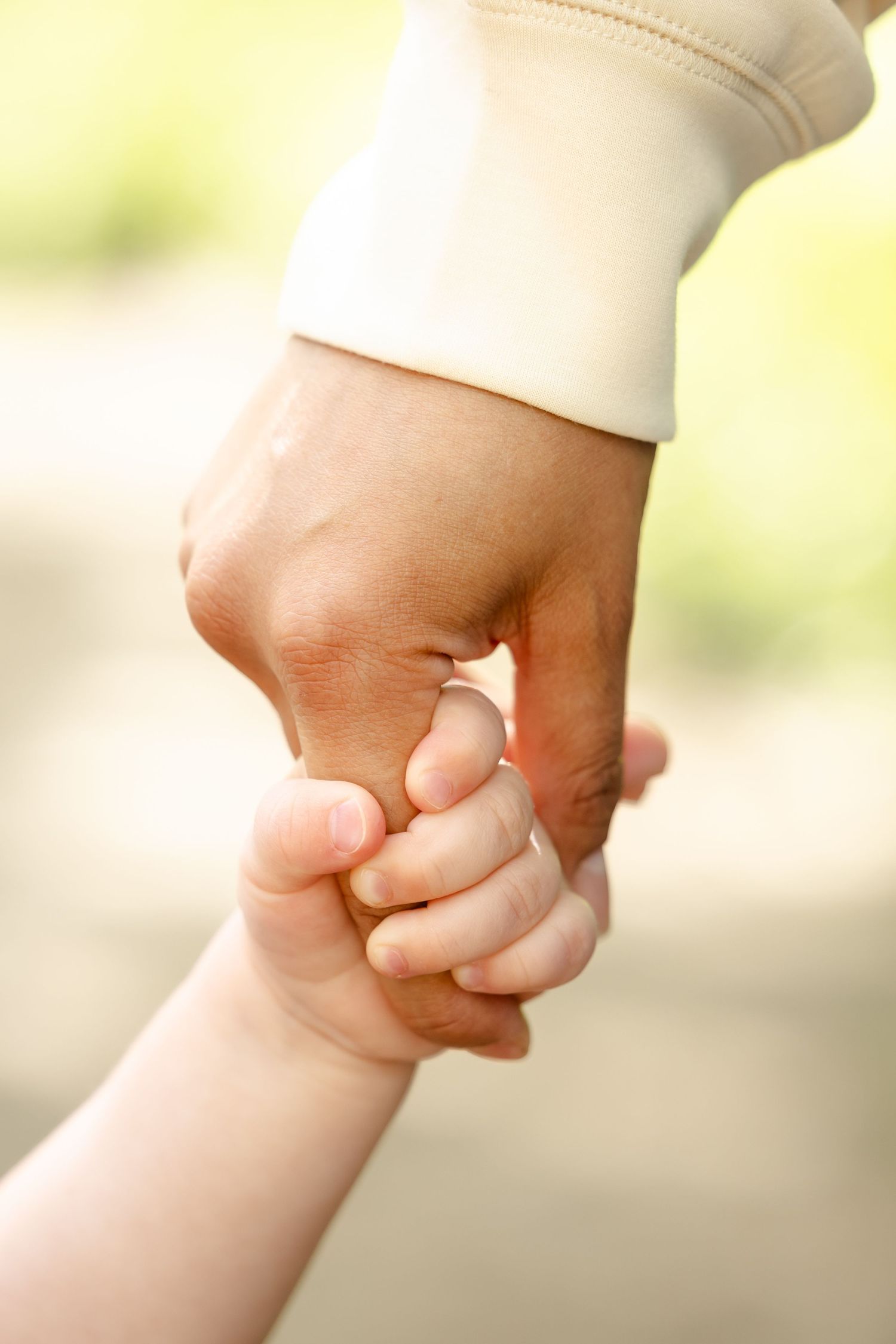 An adult hand gently holding a small child's hand outdoors, symbolizing parental love and protection.