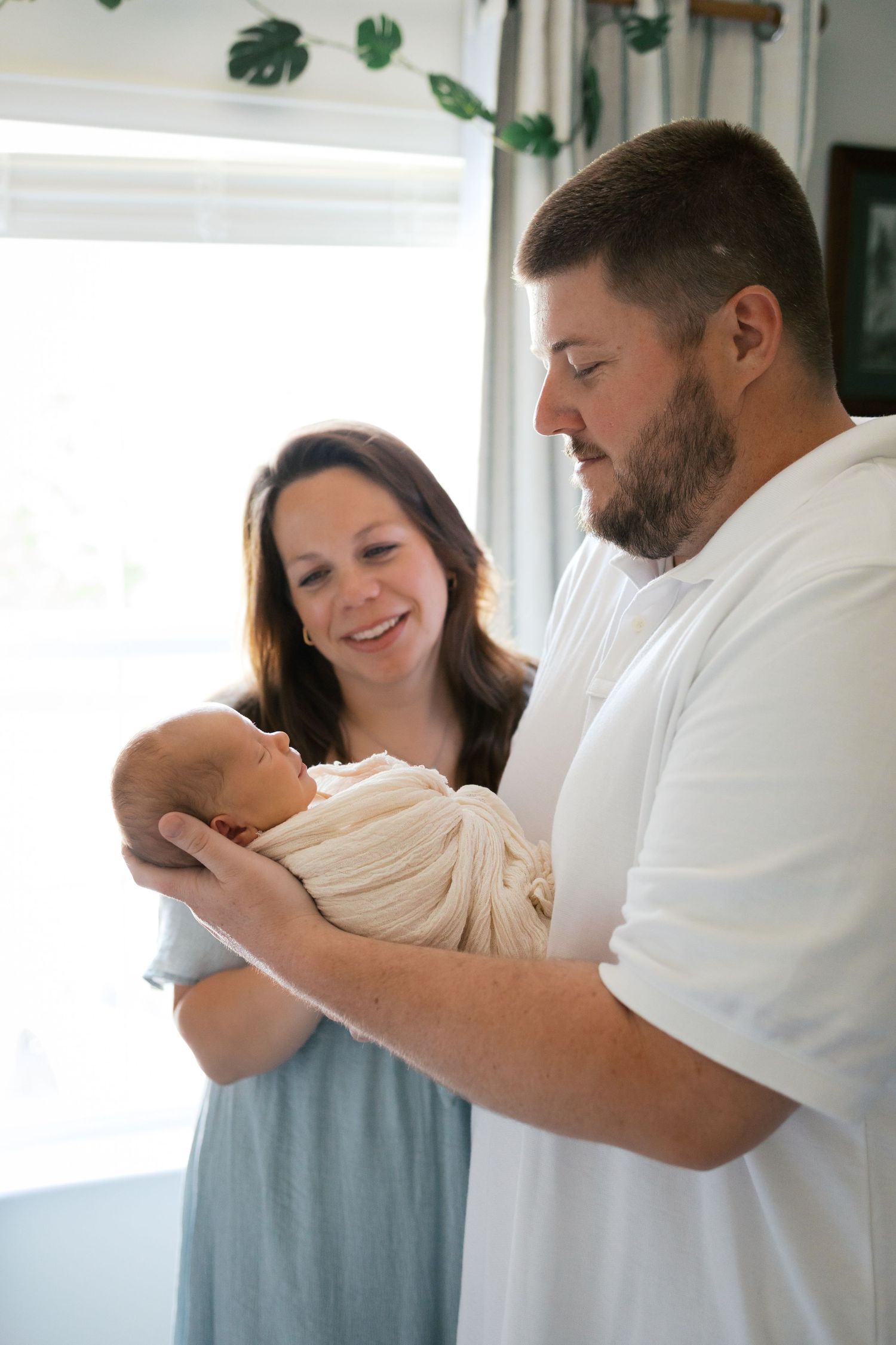 A smiling couple lovingly gazes at their newborn during Brownsburg, Indiana Lifestyle Newborn Session by Katy Rose Photography.