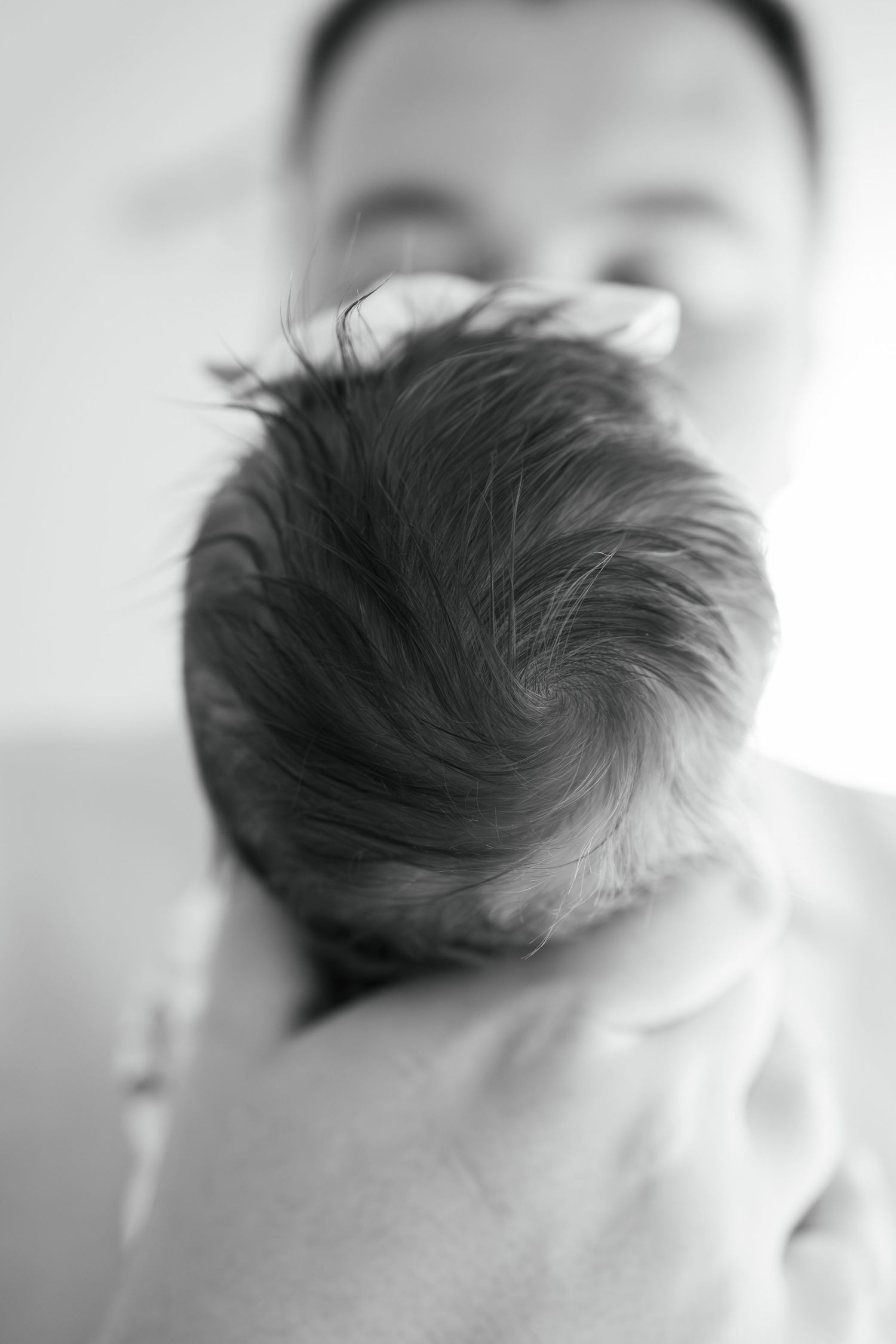 Black and white photo of a newborn baby's head with dark hair, cradled in a parent's hands.