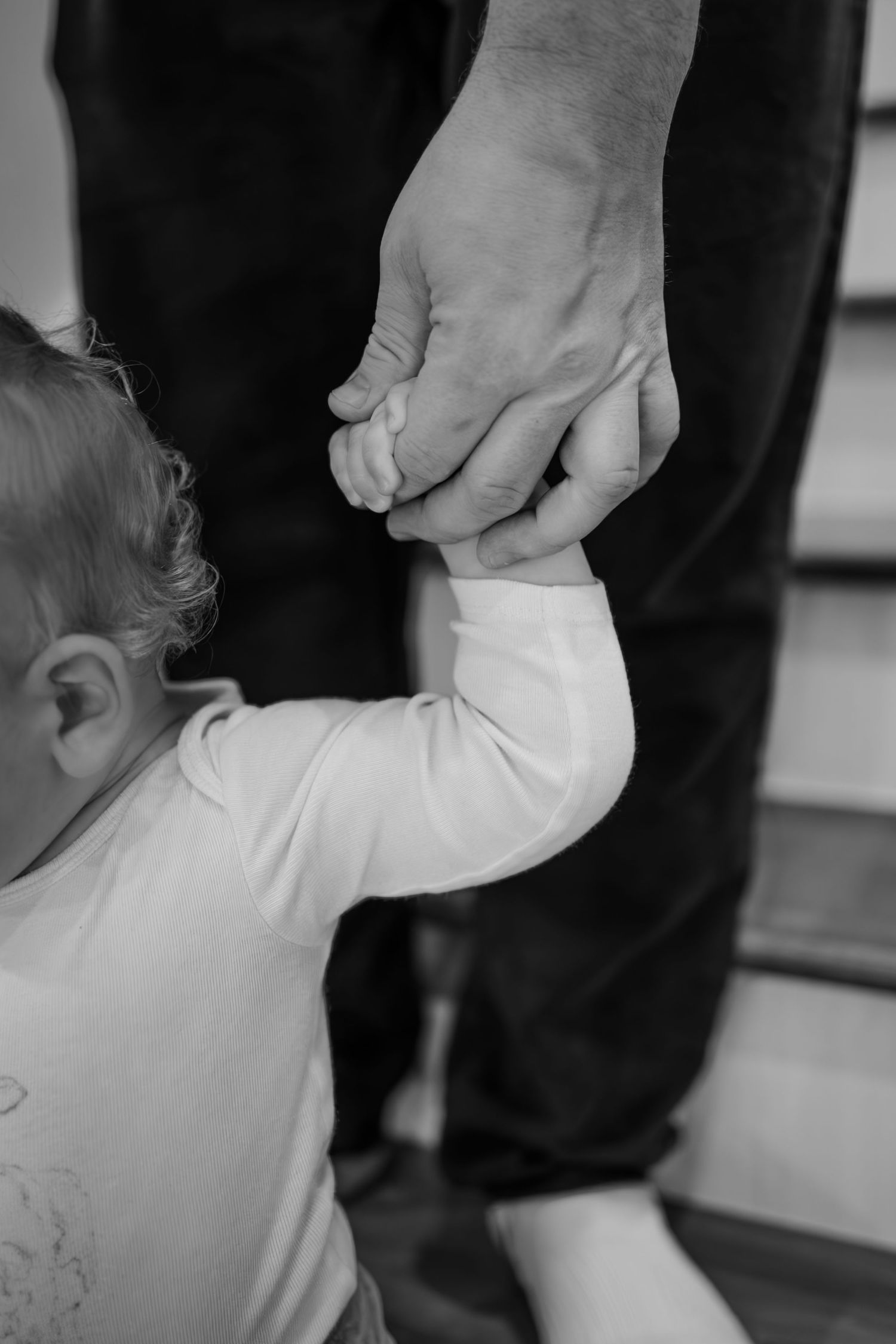 Black and white image of a child's hand wrapped around father's finger during in-home lifestyle family photoshoot in Whitestown, Indiana