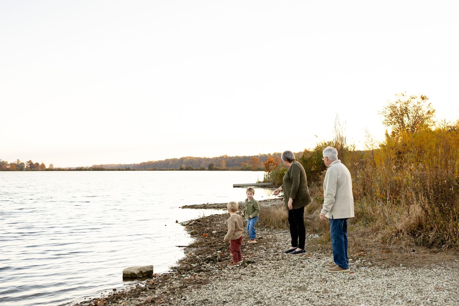 Silhouettes of people walking along a rocky lakeshore at sunset during family portrait session at Eagle Creek State Park in Indianapolis.