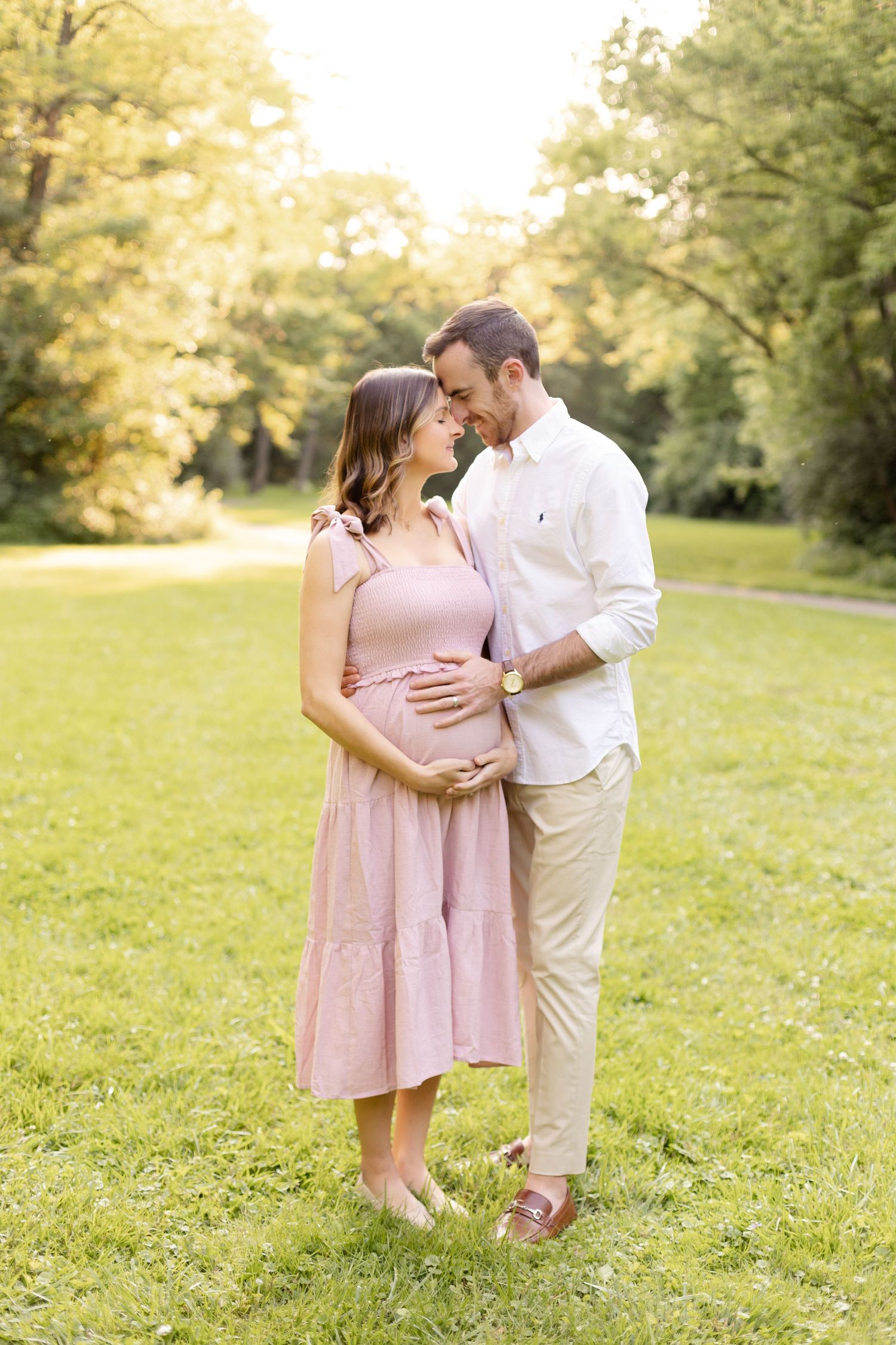 Romantic maternity photo of couple embracing in sunlit garden setting.