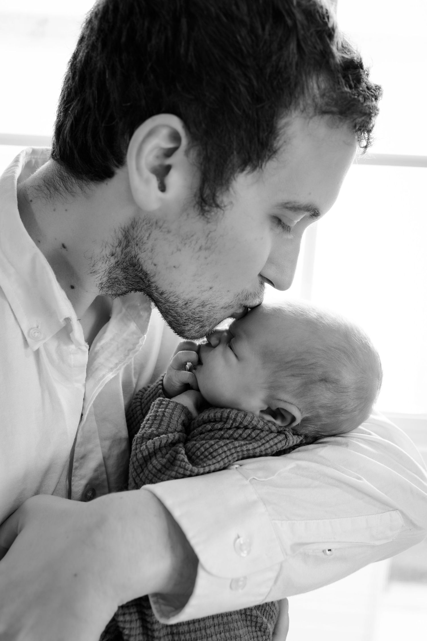 Father gently kissing their sleeping infant's head during in-home newborn session in Indianapolis by Katy Rose Photography.