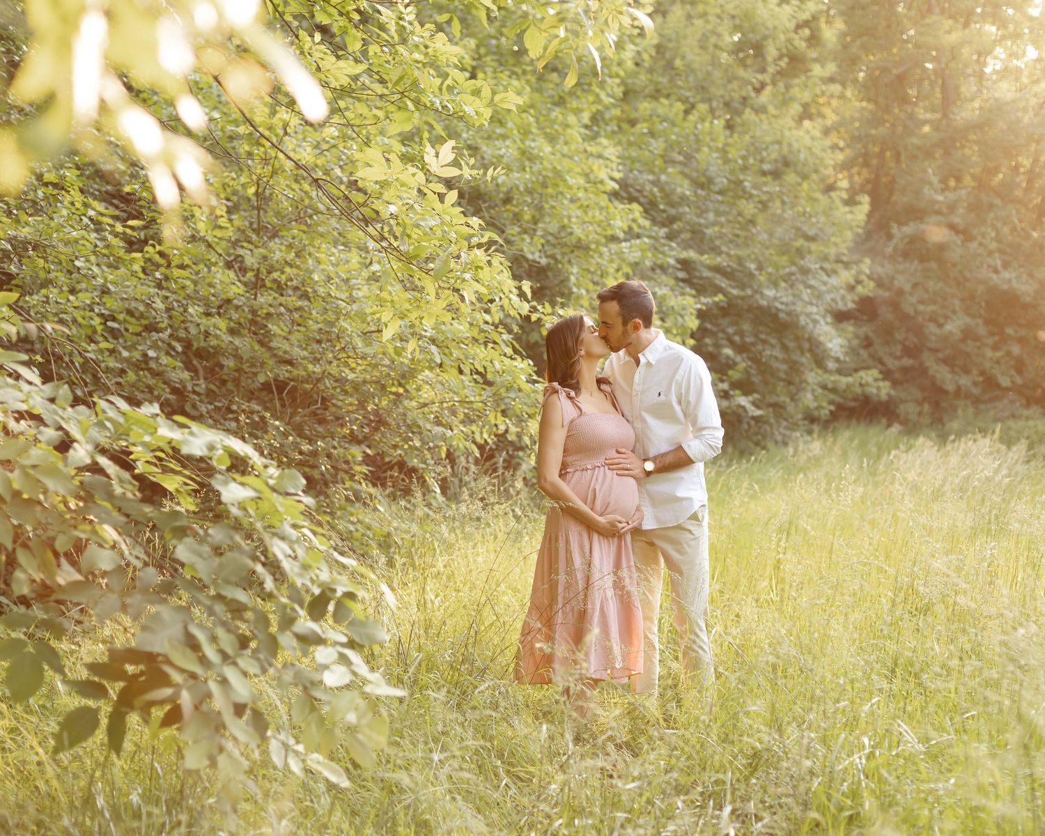 Dreamy sunset maternity photo of couple embracing in golden field.