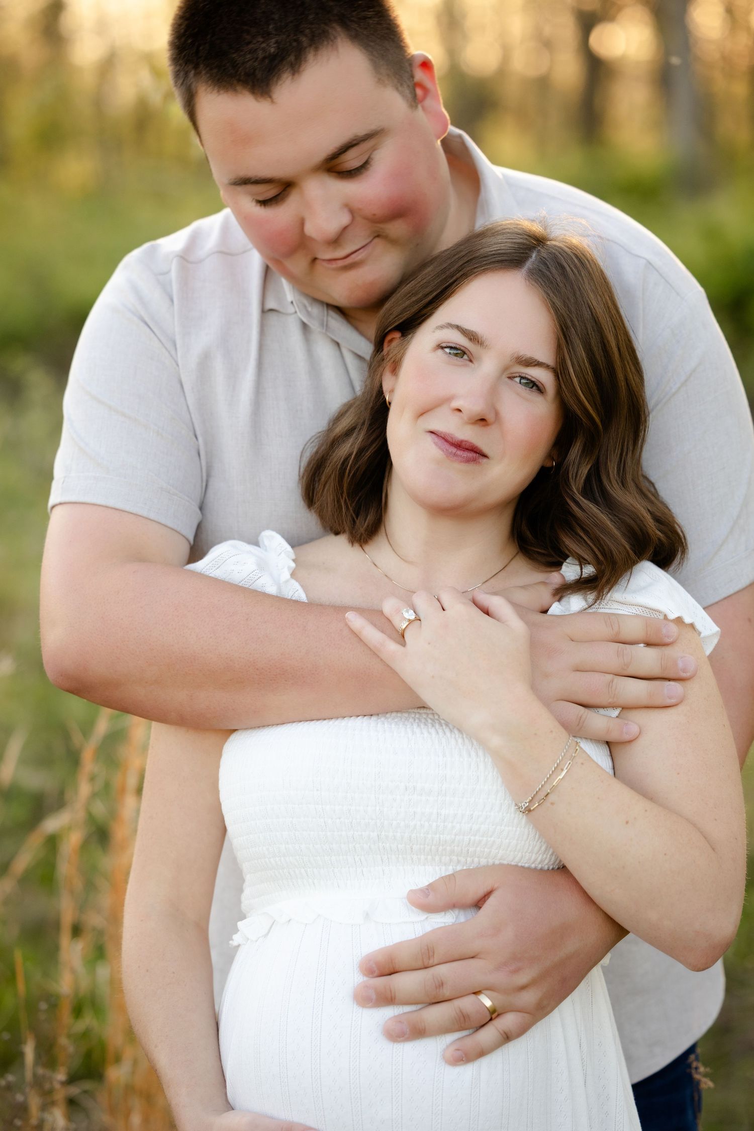 A man tenderly embraces a pregnant woman in a white dress during their maternity photos in Avon, Indiana by Katy Rose Photography.