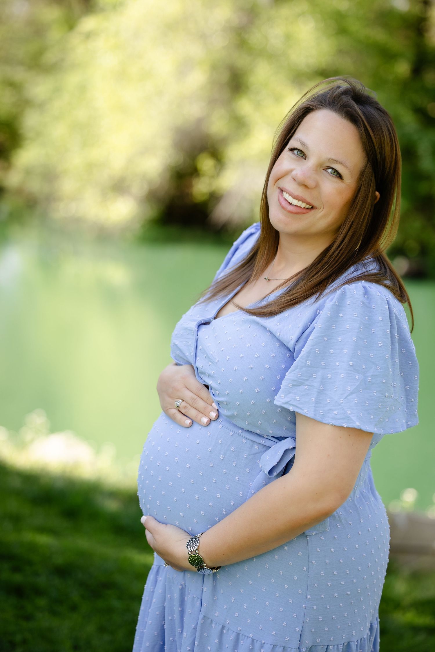 Smiling pregnant woman in blue dress cradling baby bump at Avon Gardens during maternity session by Katy Rose Photography.