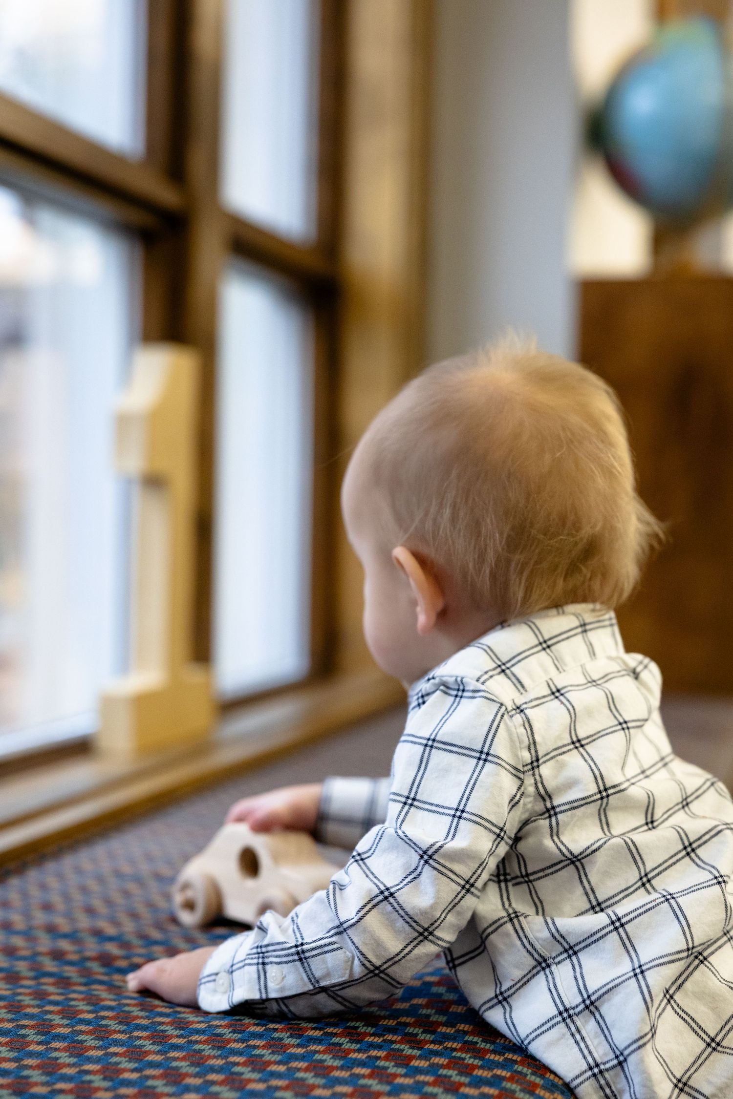 Baby in checkered shirt lying on patterned carpet near windows for first birthday session in Zionsville, IN by Katy Rose Photography.