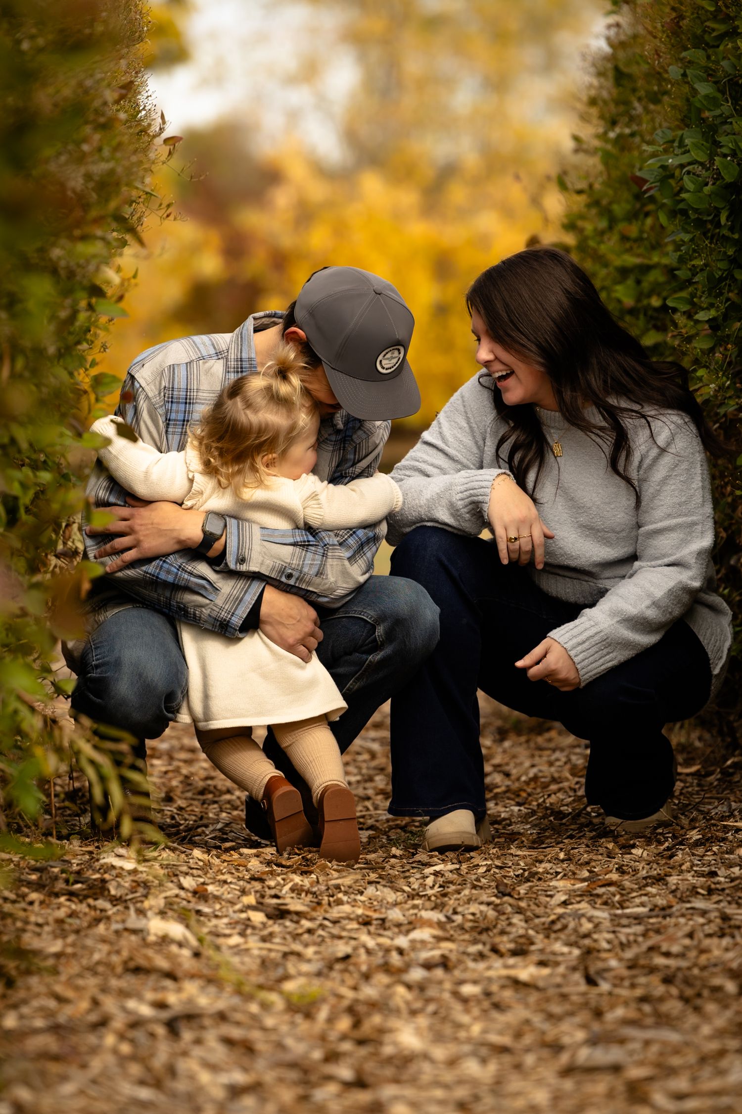 A playful family photo sequence showing interaction on fallen leaves between garden hedges during family session in Hendricks County.