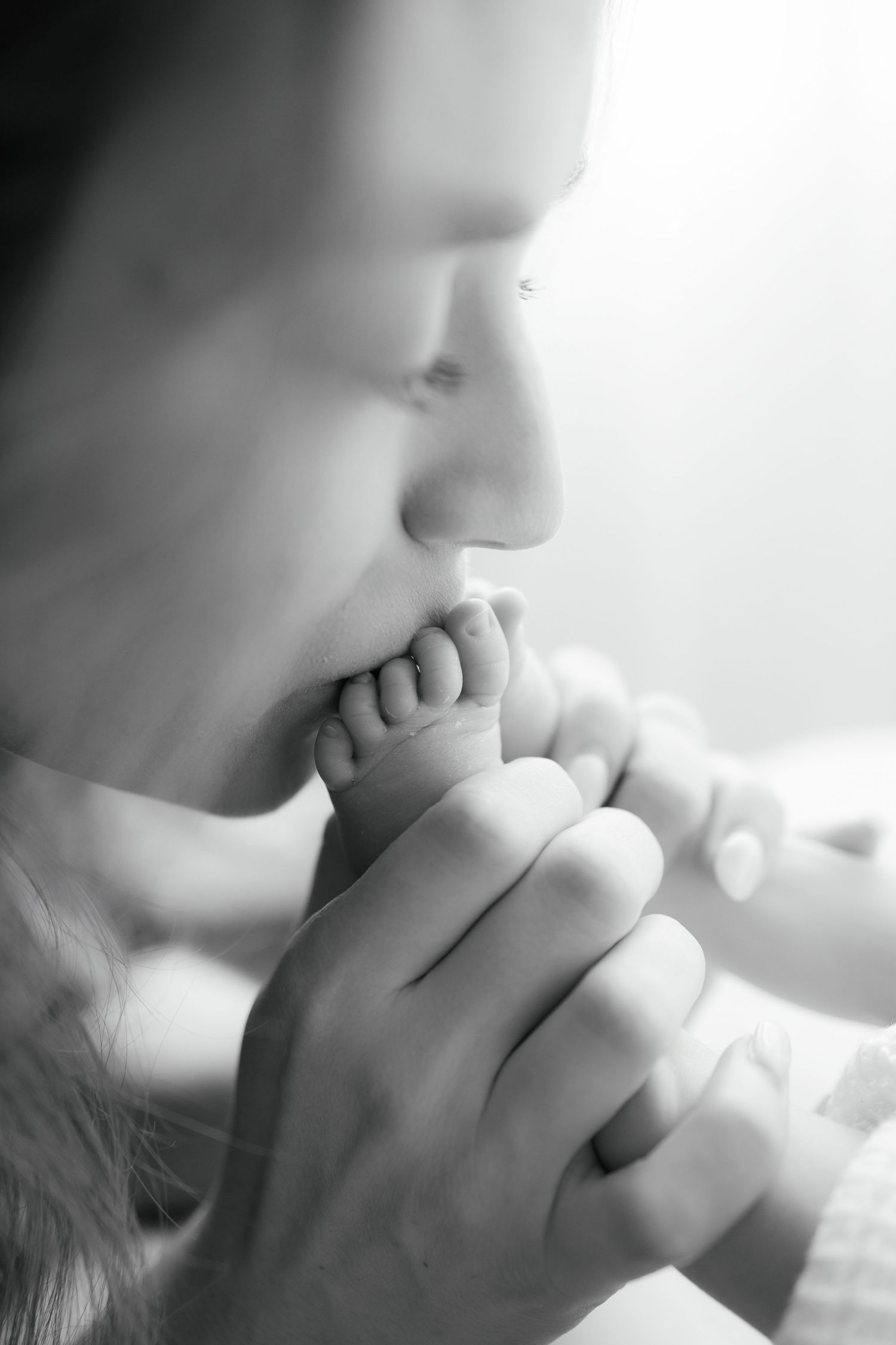 Black and white photo of a parent tenderly kissing a newborn baby's tiny feet, capturing a precious bonding moment.