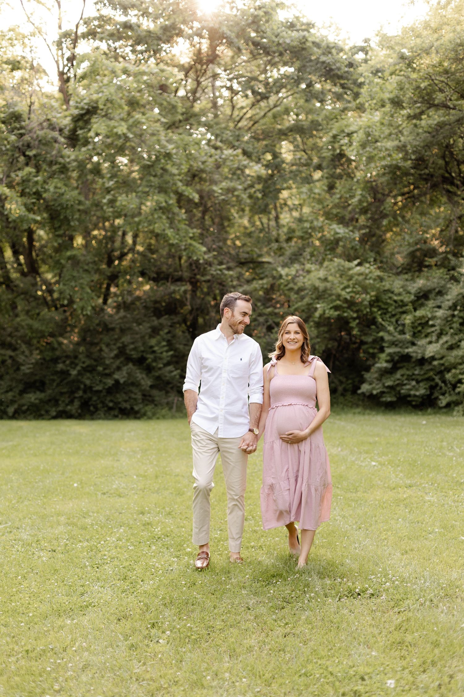 Couple walking hand in hand through a green summer meadow during maternity session by Katy Rose Photography.