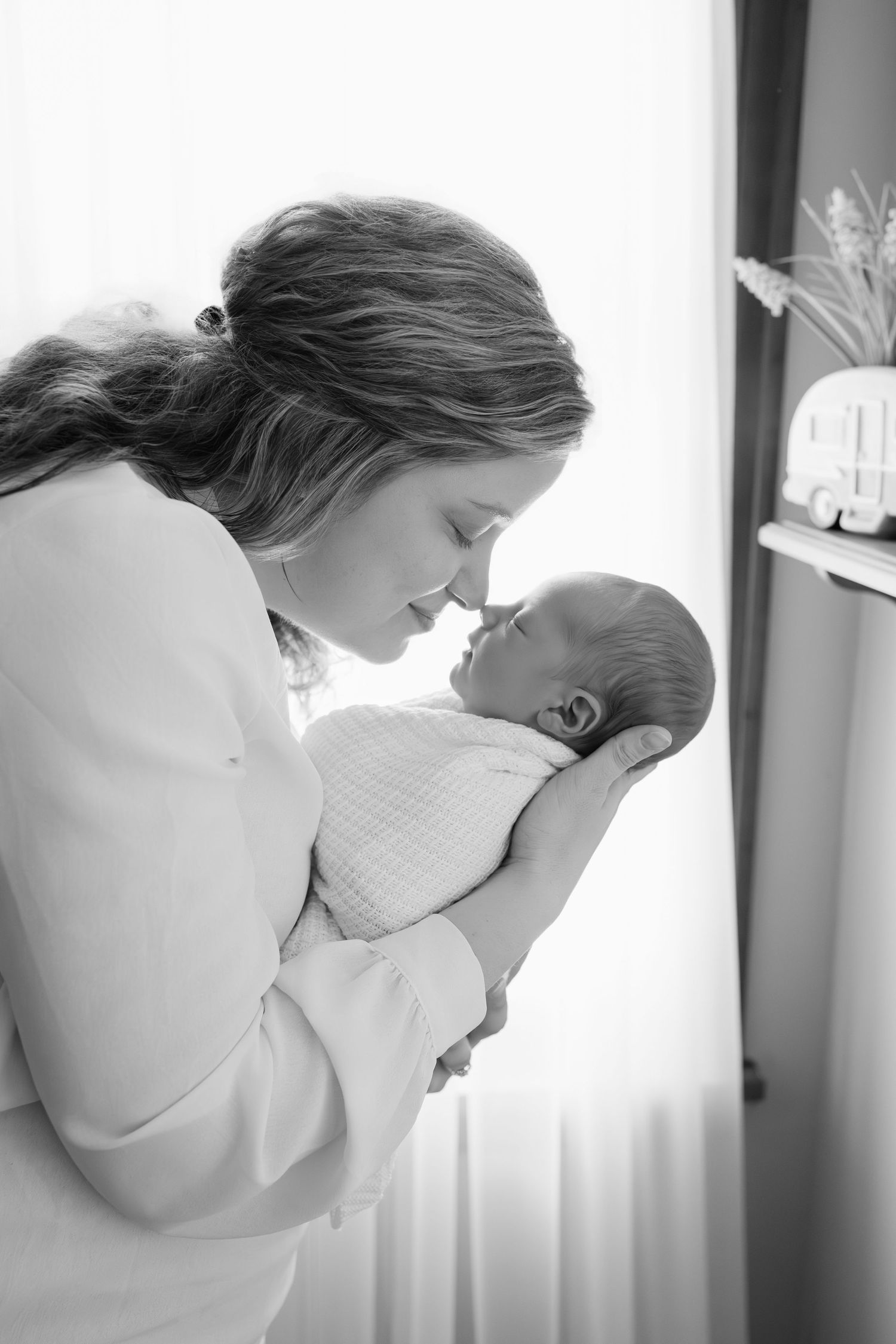 Black and white photo of a mother tenderly holding her newborn baby close, touching noses during Indianapolis in-home newborn session.