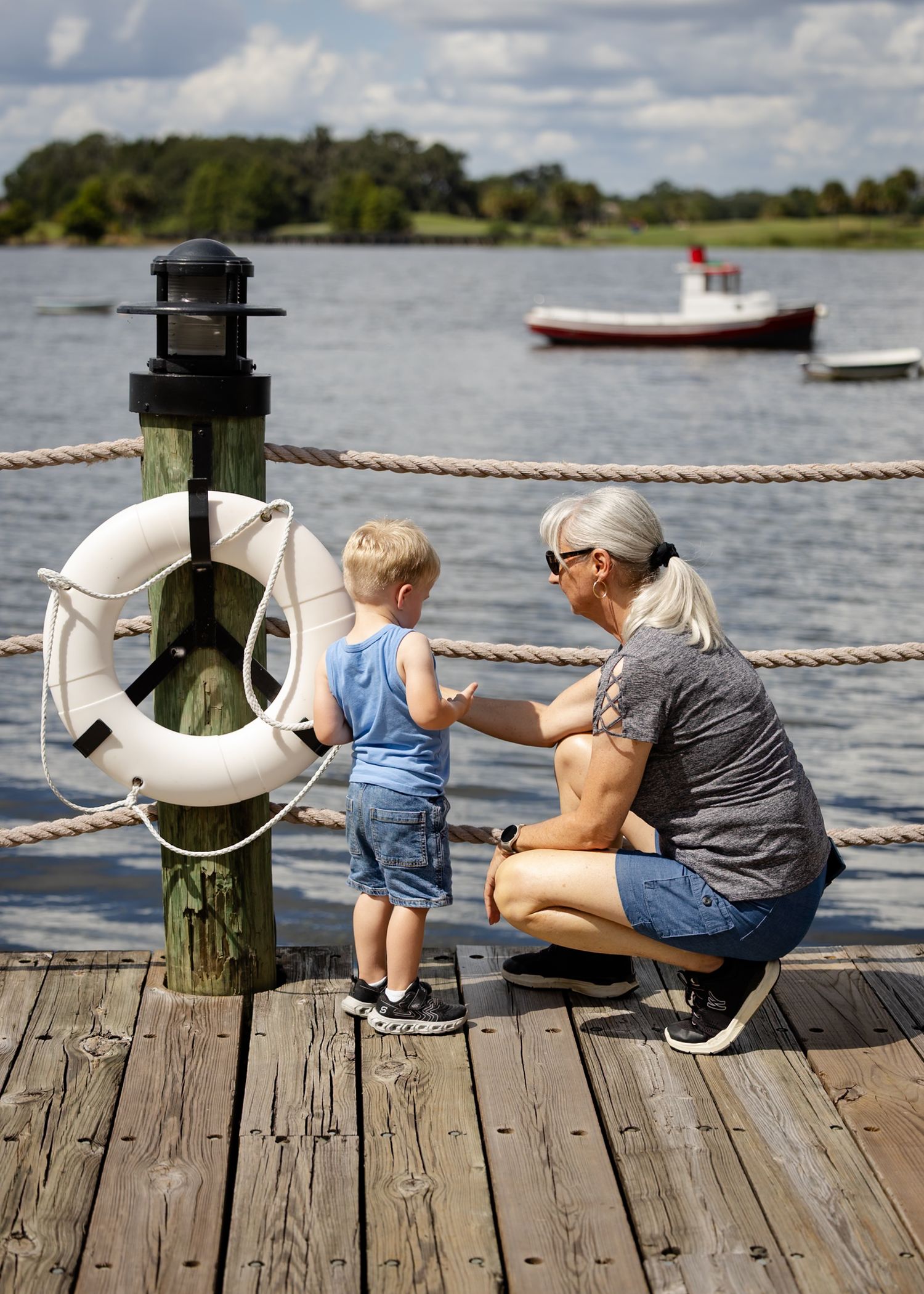 A peaceful scene of a grandmother and grandson sitting on a wooden dock overlooking the water on a sunny day by Katy Rose Photography.