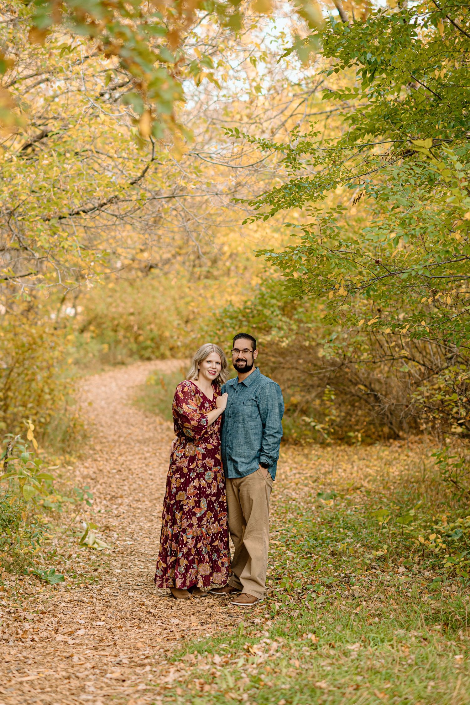 Couple embracing on a winding path surrounded by golden autumn foliage.