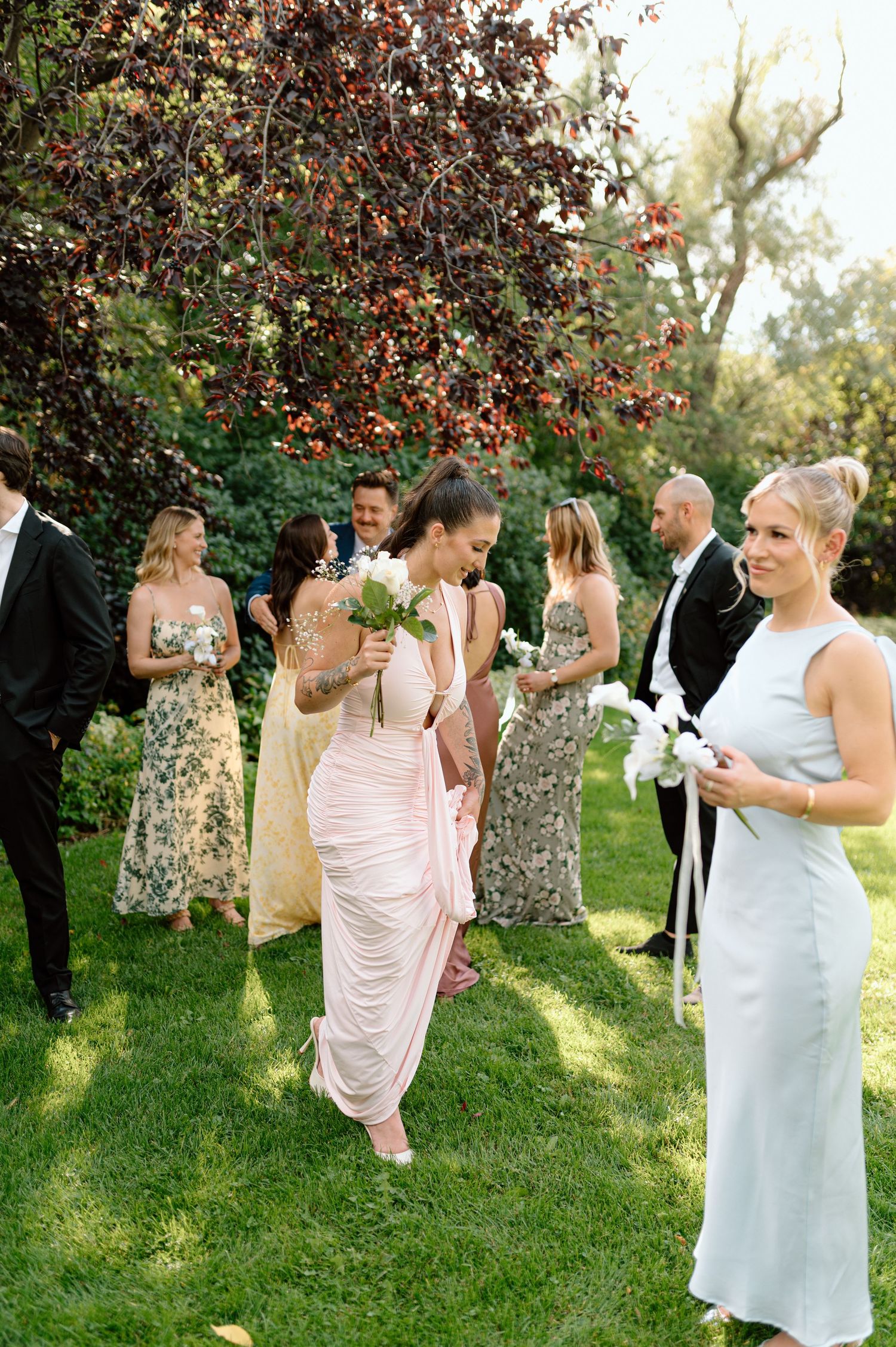 Bridesmaids in pastel gowns walking with white bouquets during outdoor wedding party photos.