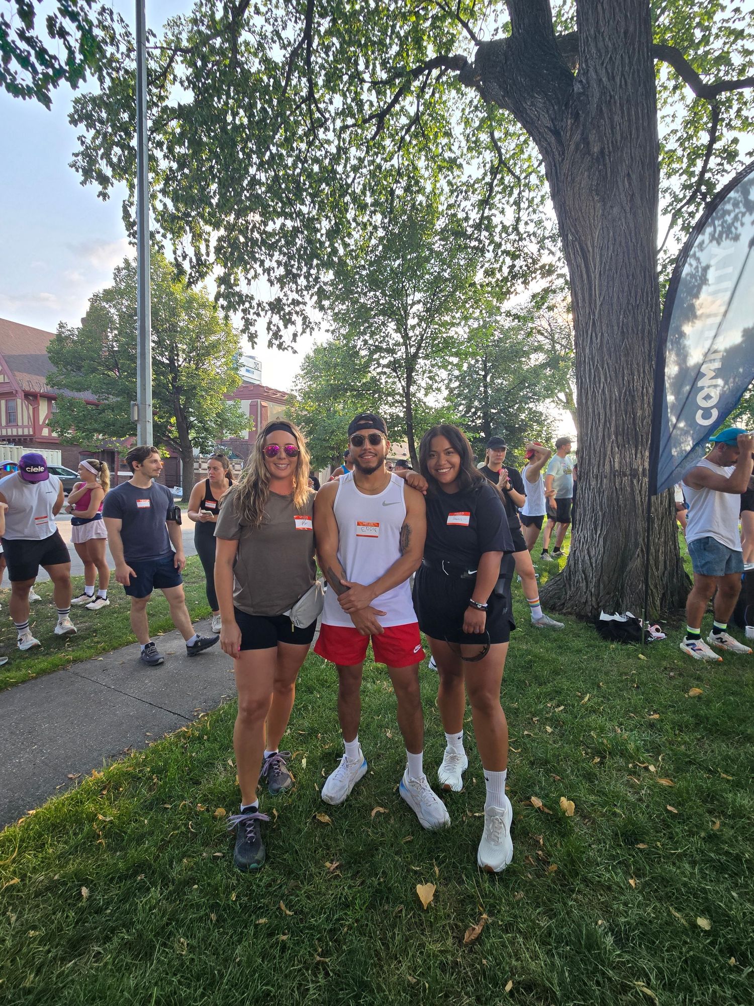Three friends posing together at outdoor fitness event under shady tree.
