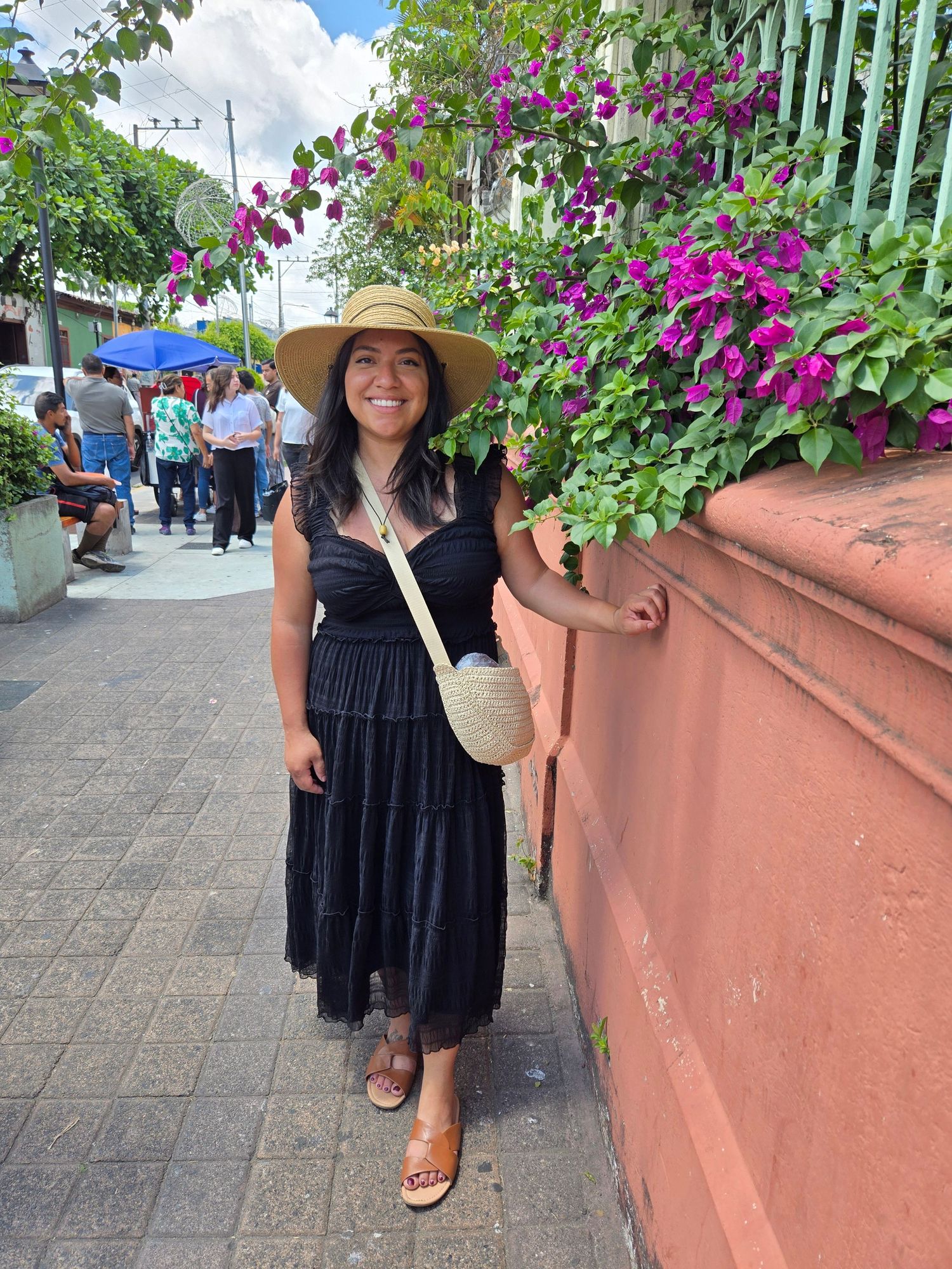Woman in black dress and straw hat posing beside vibrant bougainvillea flowers.