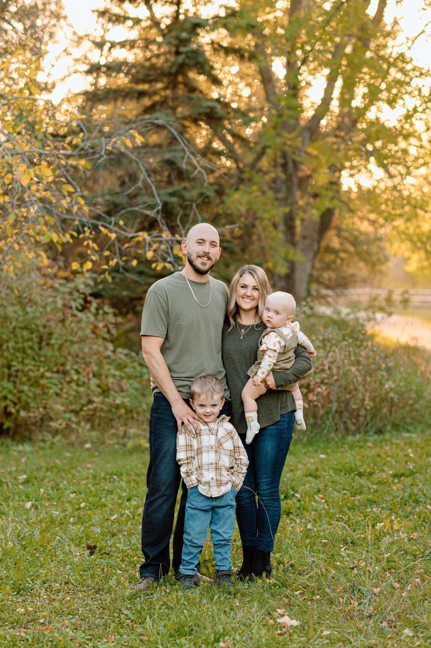 Happy family of four poses together in a sunlit autumn meadow surrounded by colorful fall foliage.