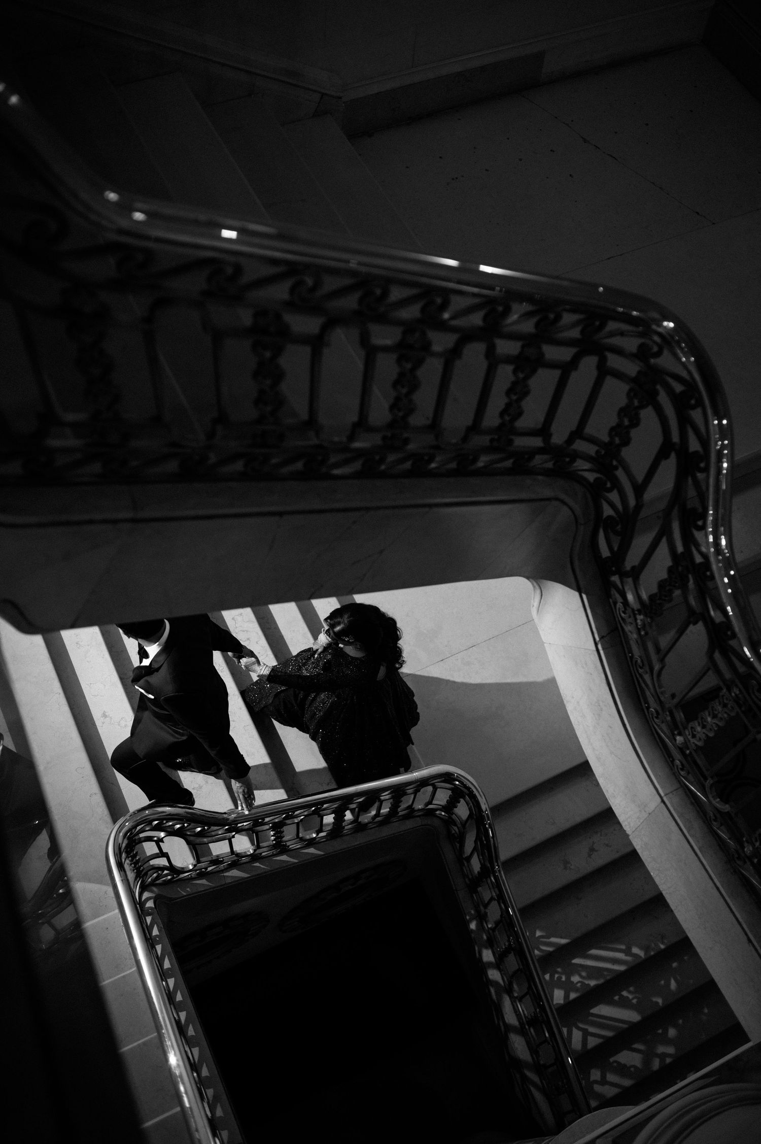 Dramatic black and white overhead shot of a couple on an ornate spiral staircase.