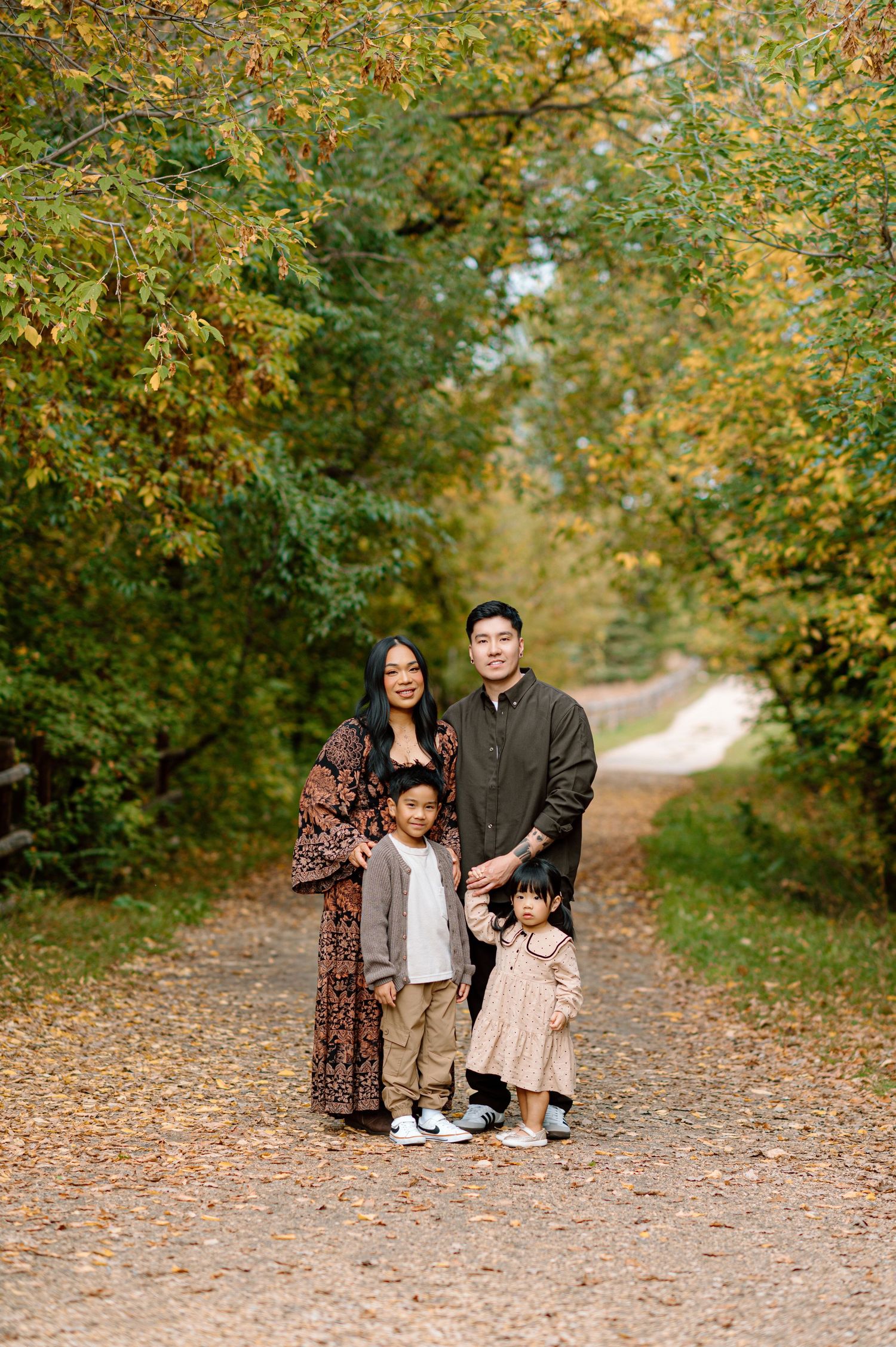 Family of four posing on a leaf-covered path surrounded by colorful autumn foliage in fall portrait.