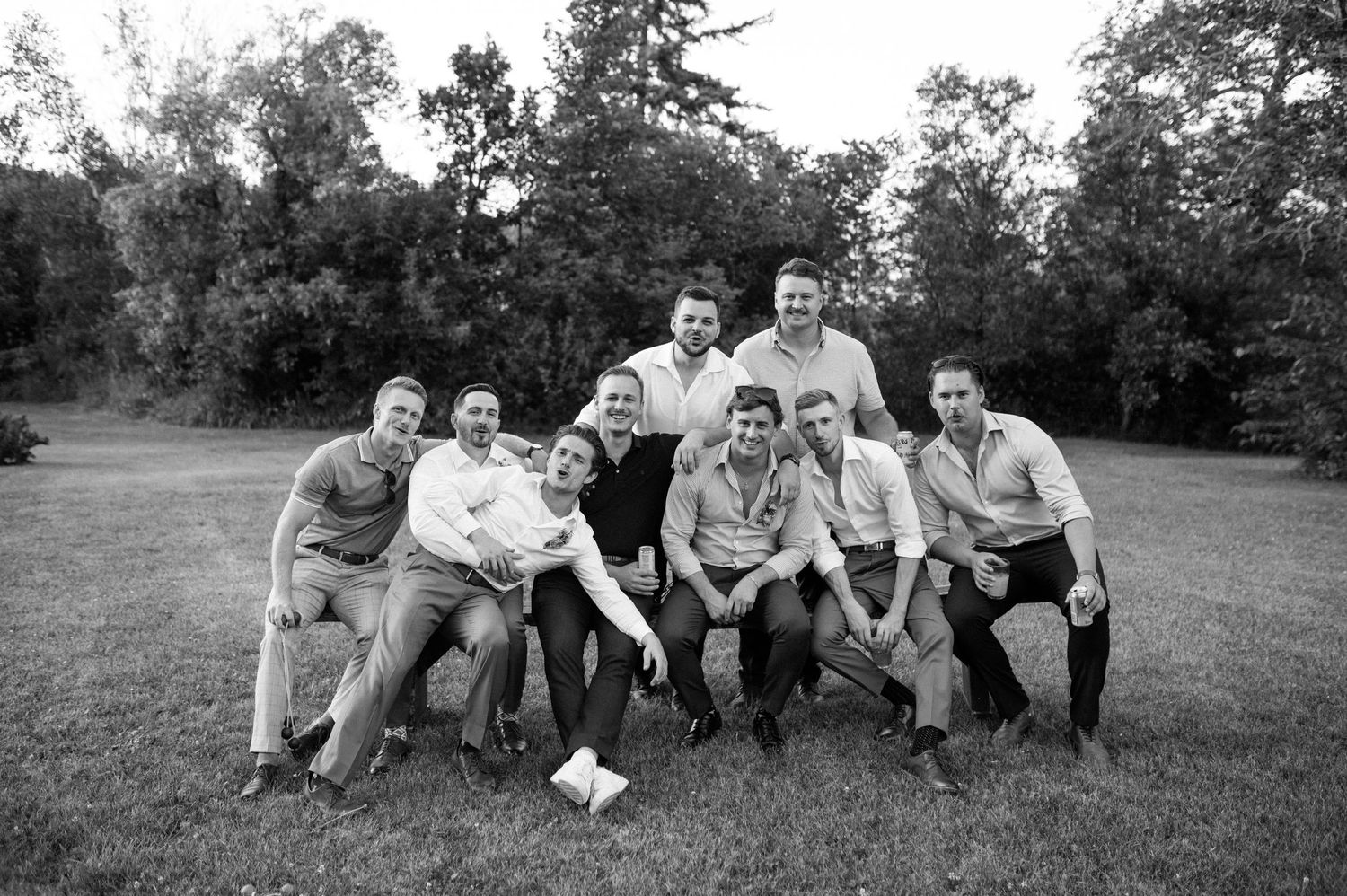 Group of groomsmen posing together outdoors in black and white wedding photo on grassy lawn.