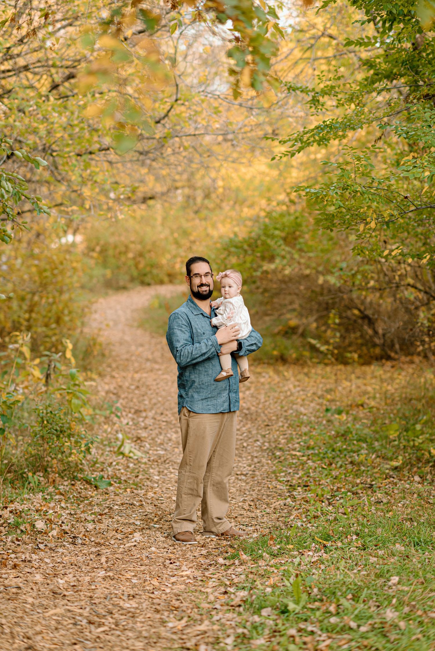 Bearded father holding baby girl on scenic autumn forest trail.