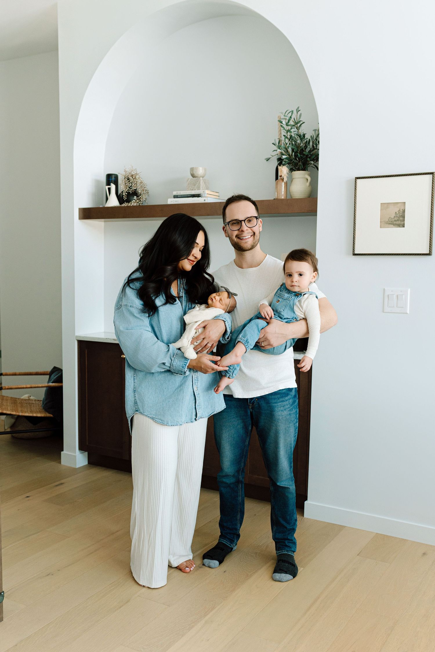 Happy family of four with newborn baby and toddler posing in modern bright home interior.