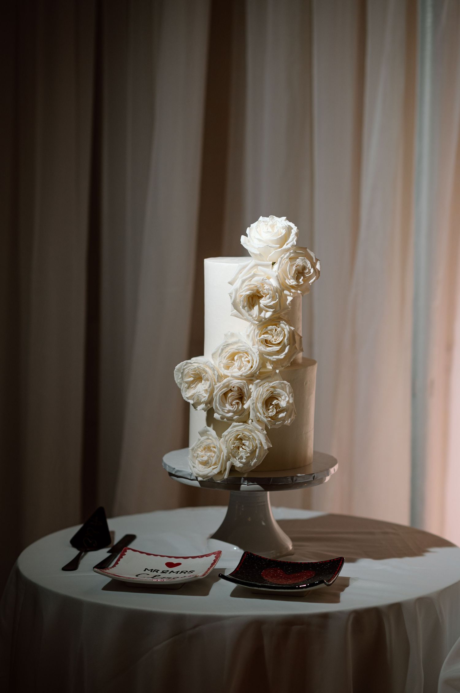 Elegant two-tier white wedding cake adorned with cascading ivory roses on a silver cake stand.