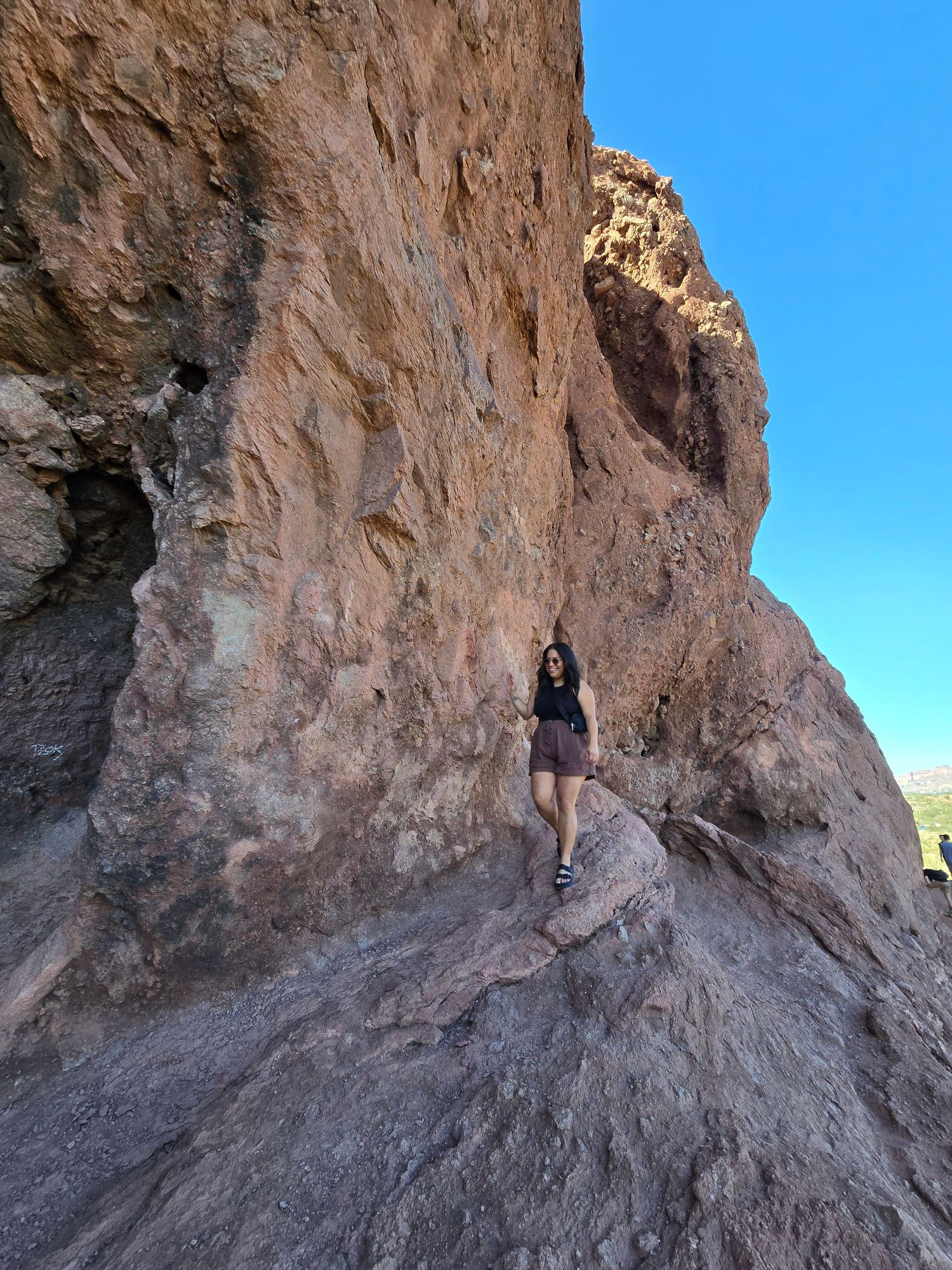 Woman hiking along narrow rocky cliff ledge in desert canyon under blue sky.