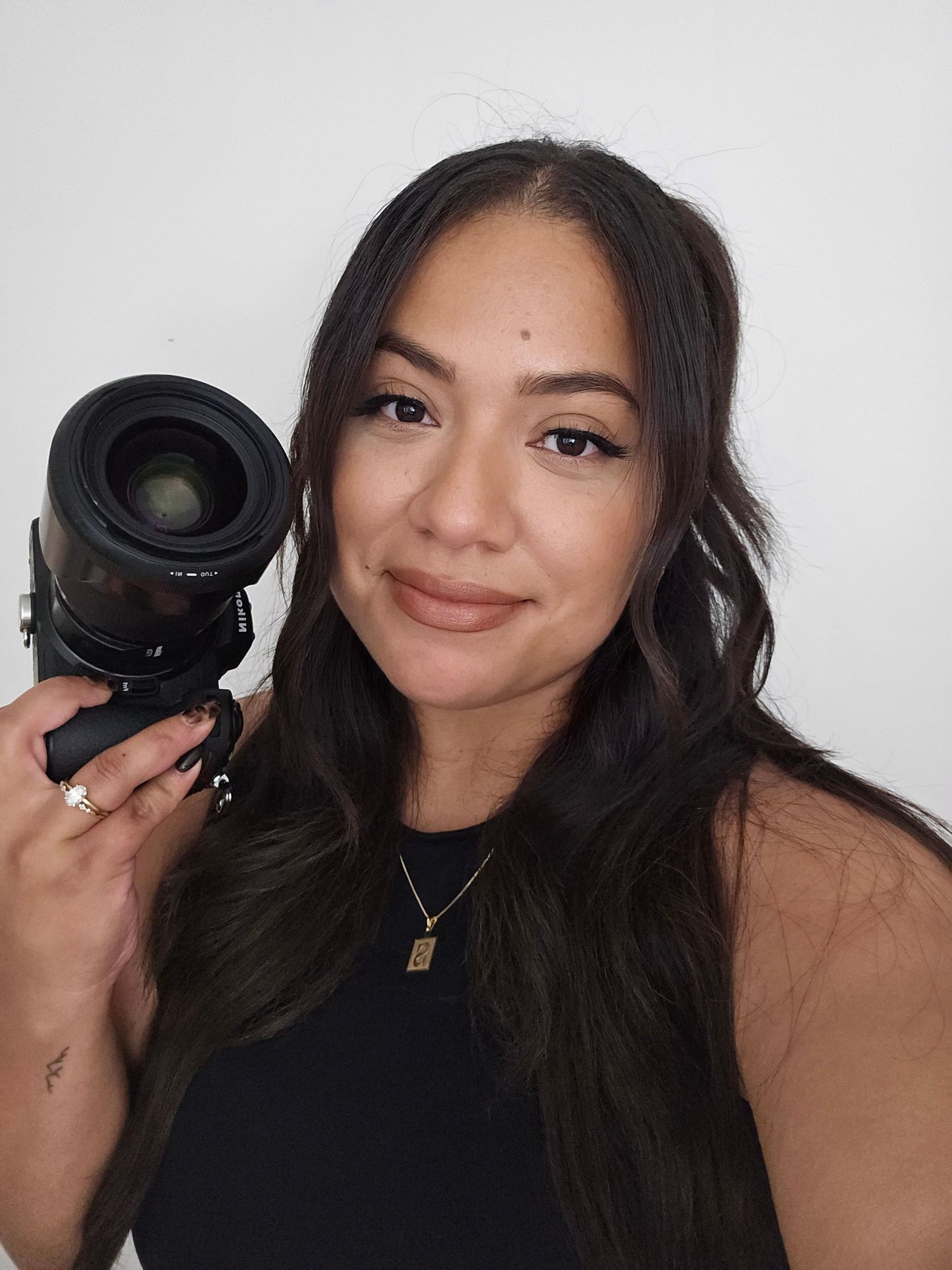 A young woman photographer smiling and holding a professional camera lens against a white background.