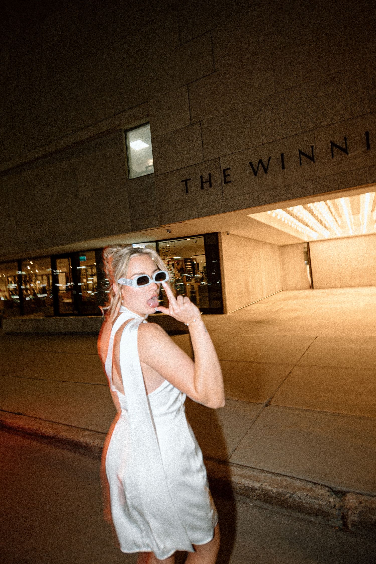 Blonde bride in white mini dress posing playfully outside The Winnipeg Art Gallery at night.