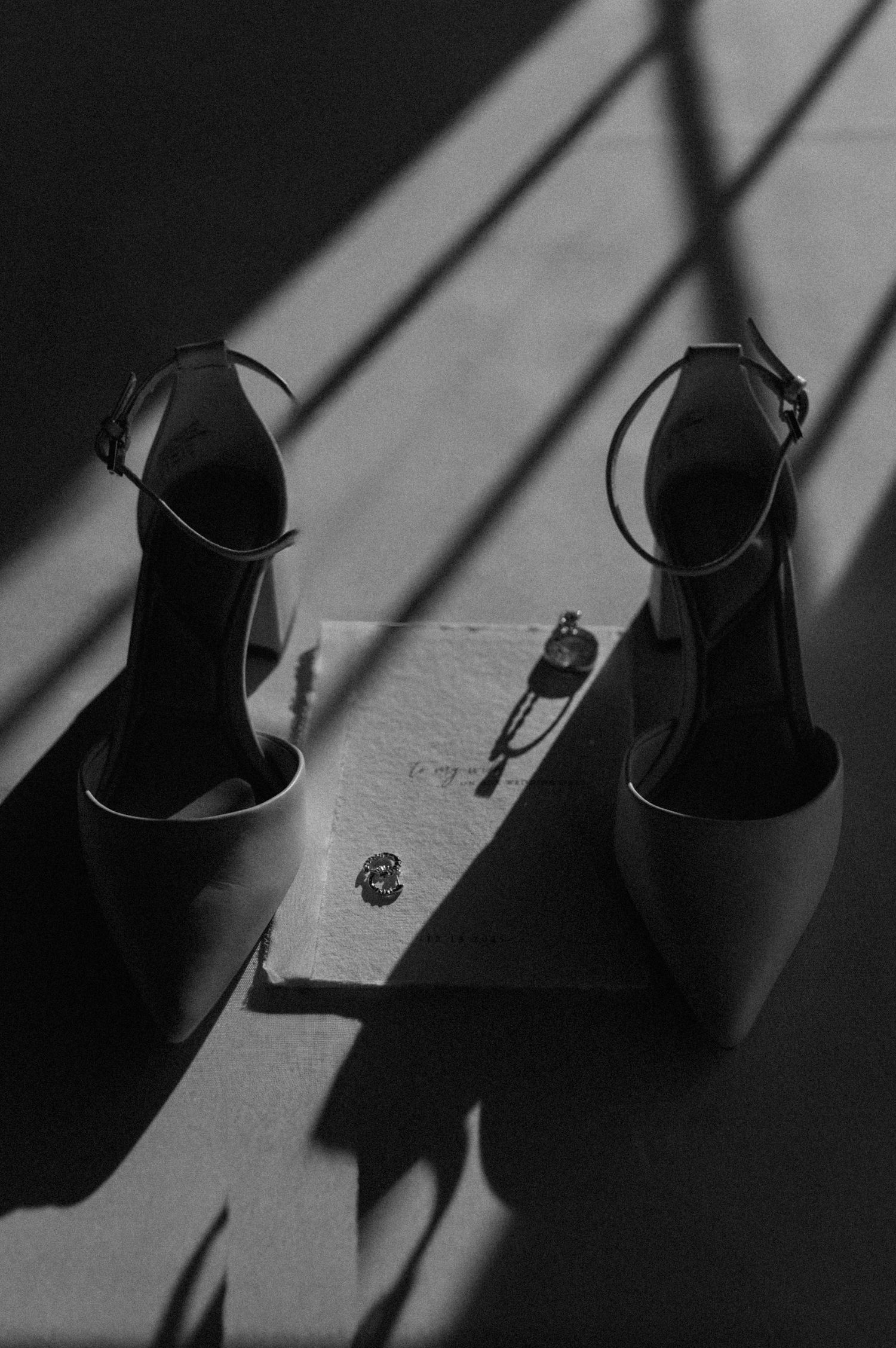 Black and white artistic photo of bridal heels and jewelry casting dramatic shadows in sunlight.