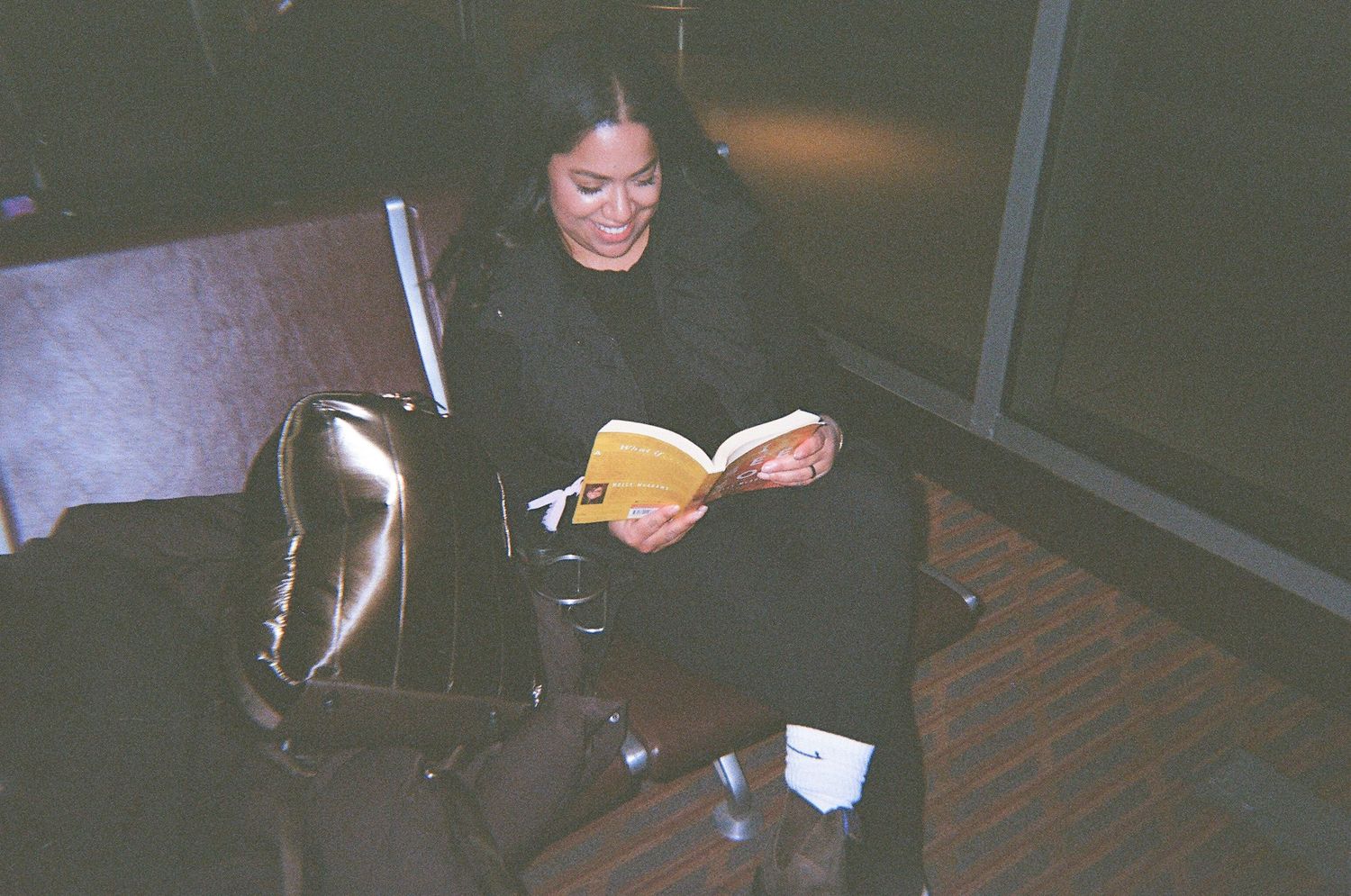 Woman reading yellow book while waiting in dark airport terminal seat.
