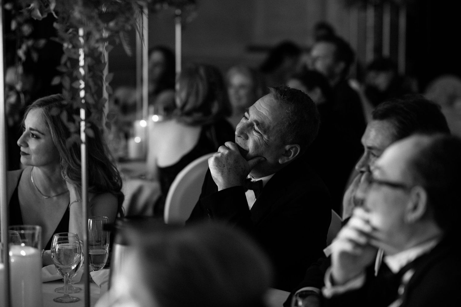 Black and white candid of wedding guests listening attentively during reception speeches at gala.
