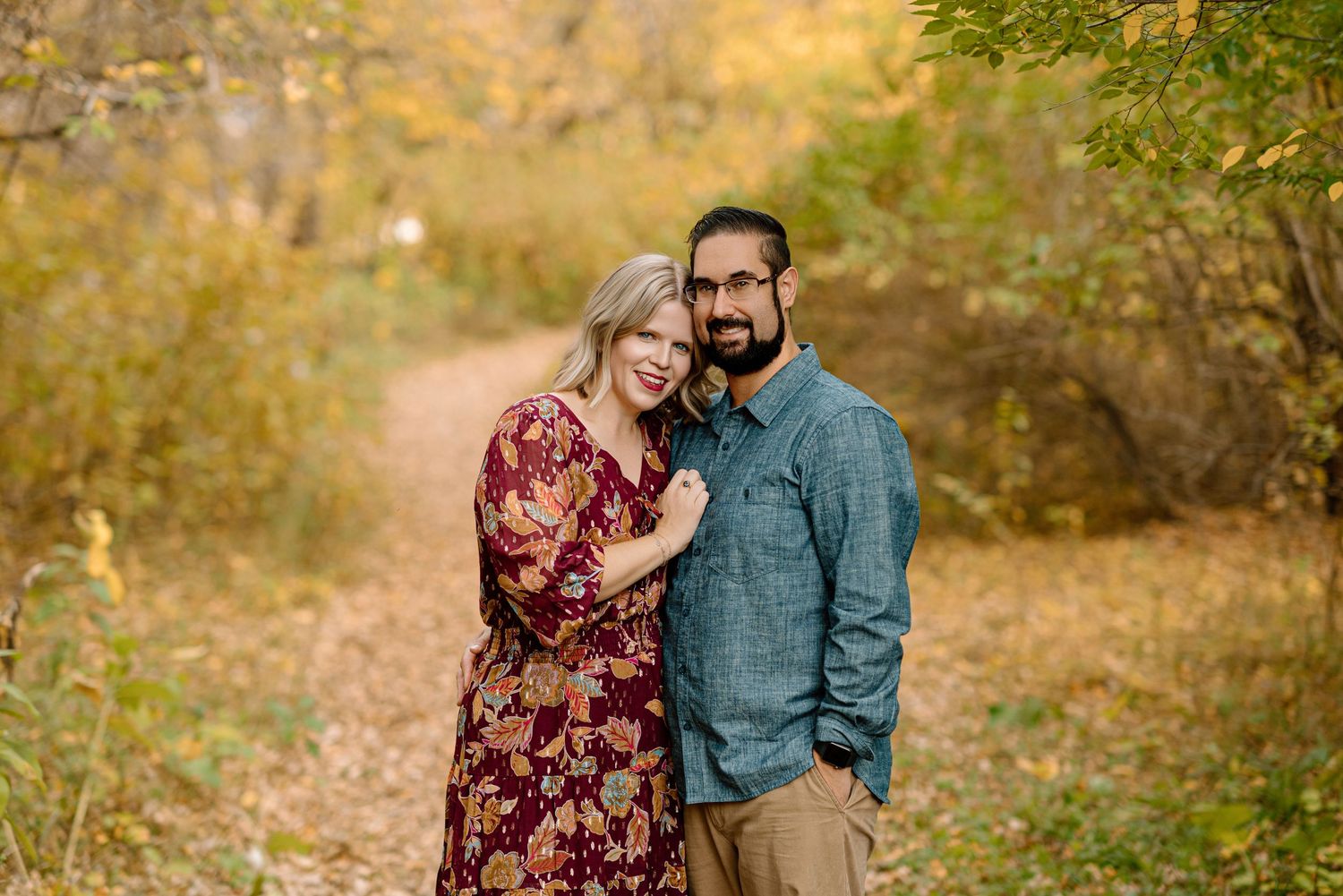 Smiling couple embracing on a path surrounded by colorful autumn foliage.